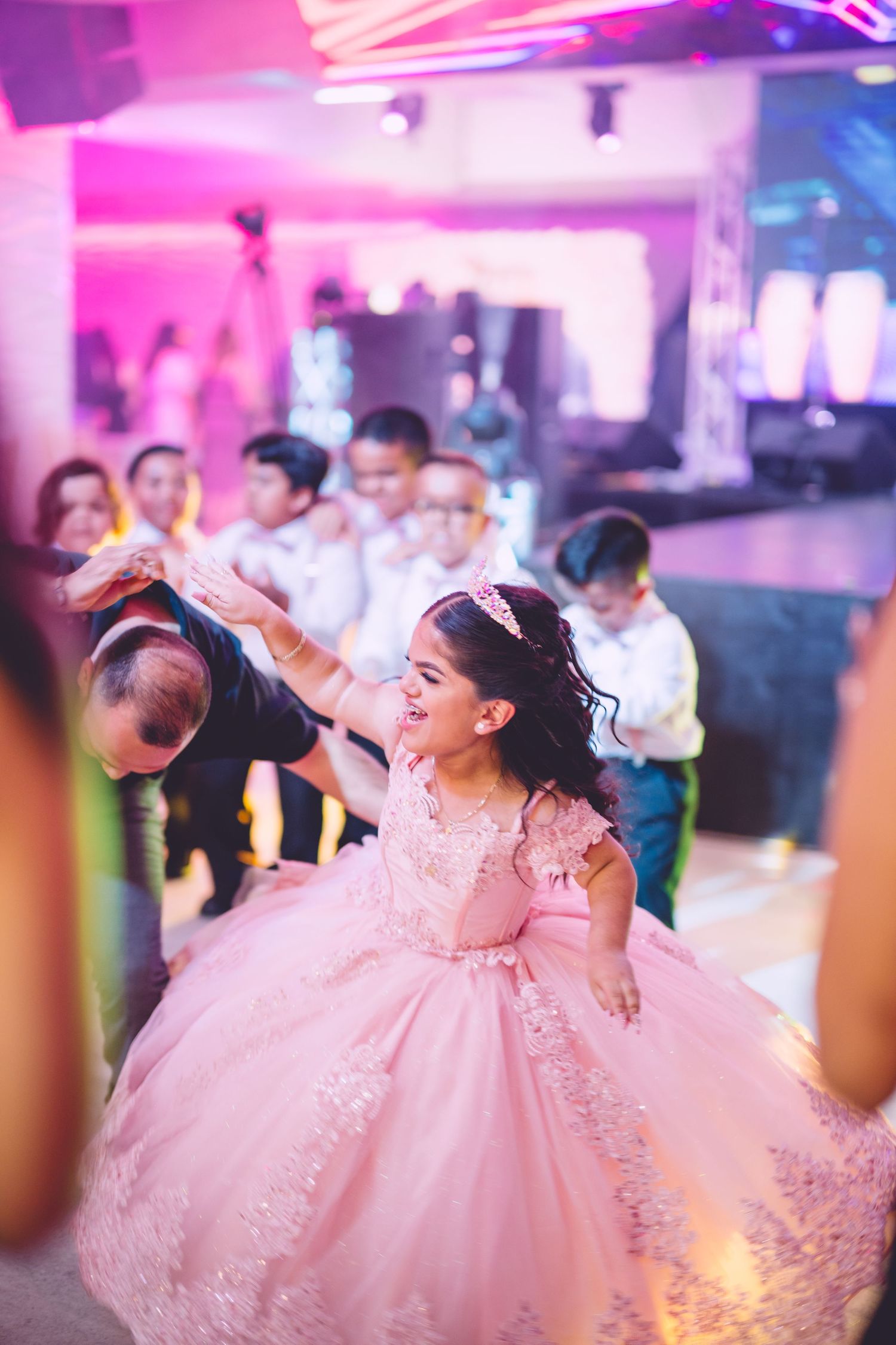 Celebration dance in pink formal gown under colorful party lighting.