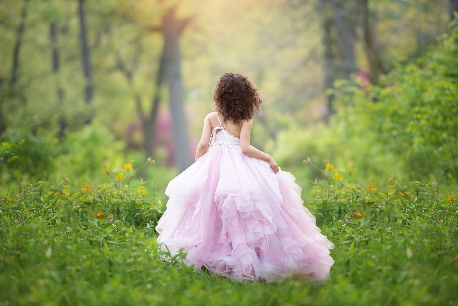 A dreamy scene in a misty forest with a girl in a flowing pink Anna Triant Couture gown walking through wildflowers.
