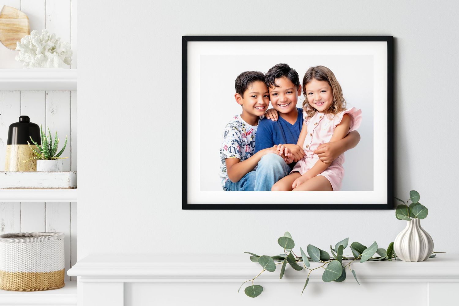 Black framed portrait photograph displayed on a white shelf with decorative eucalyptus and woven basket decor.