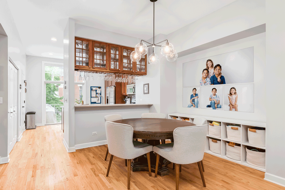 Modern dining nook with round wooden table, white chairs, built-in storage cubes and hardwood floors, modern portraits on the wall.