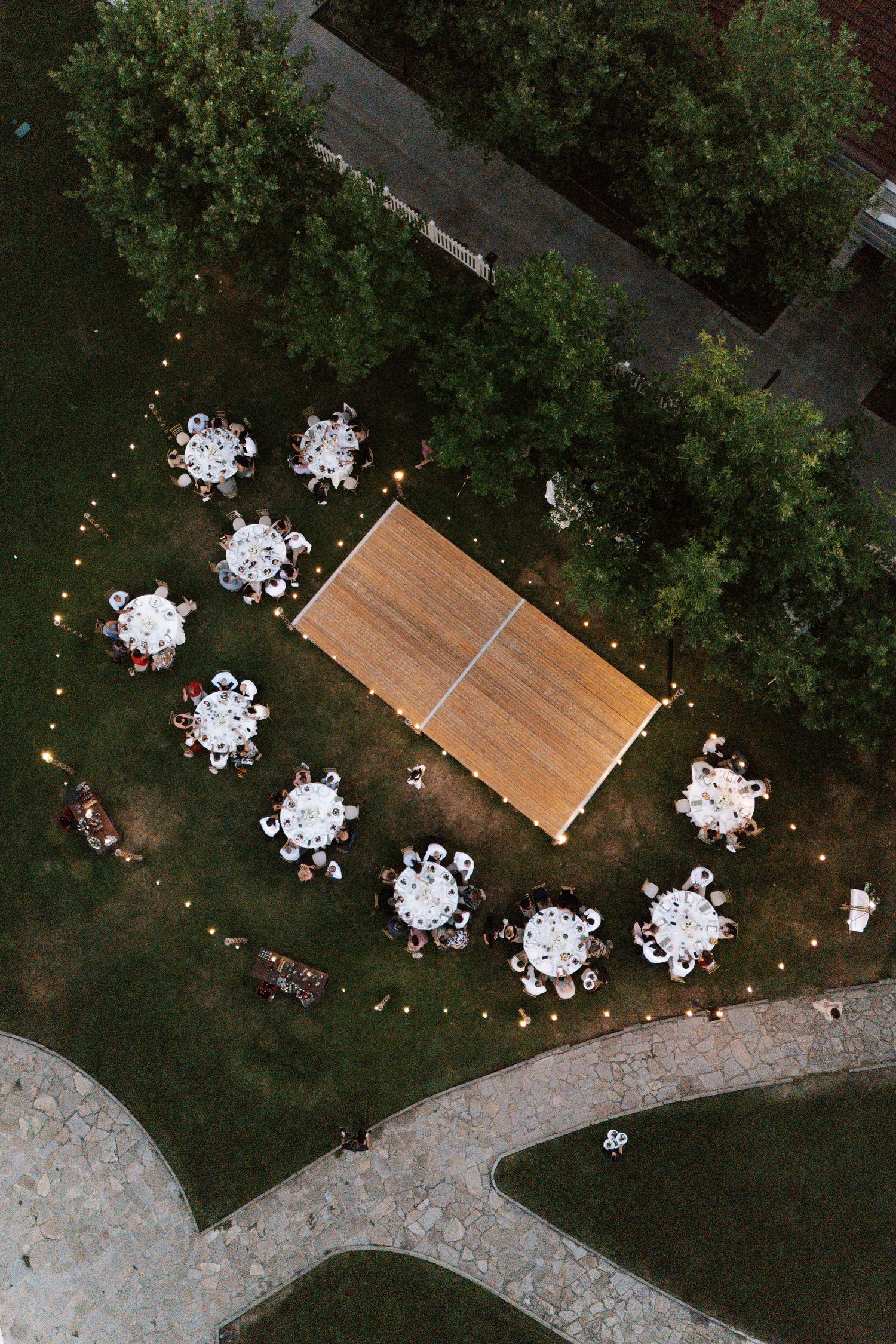 Aerial view of outdoor wedding reception tables and string lights arranged in a garden setting with stone pathway.