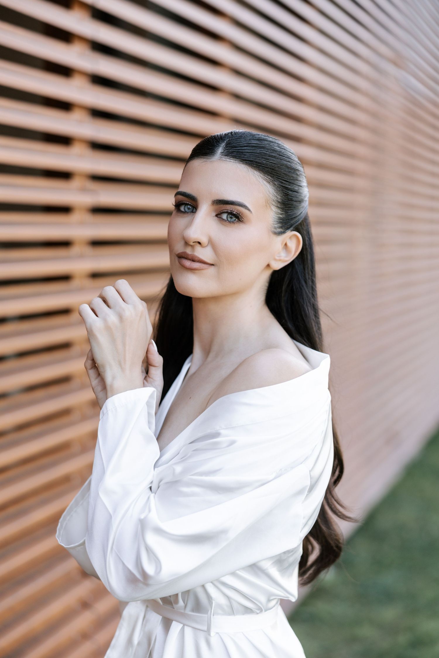 A woman in a white shirt poses against a wooden slatted wall in a series of elegant portraits.