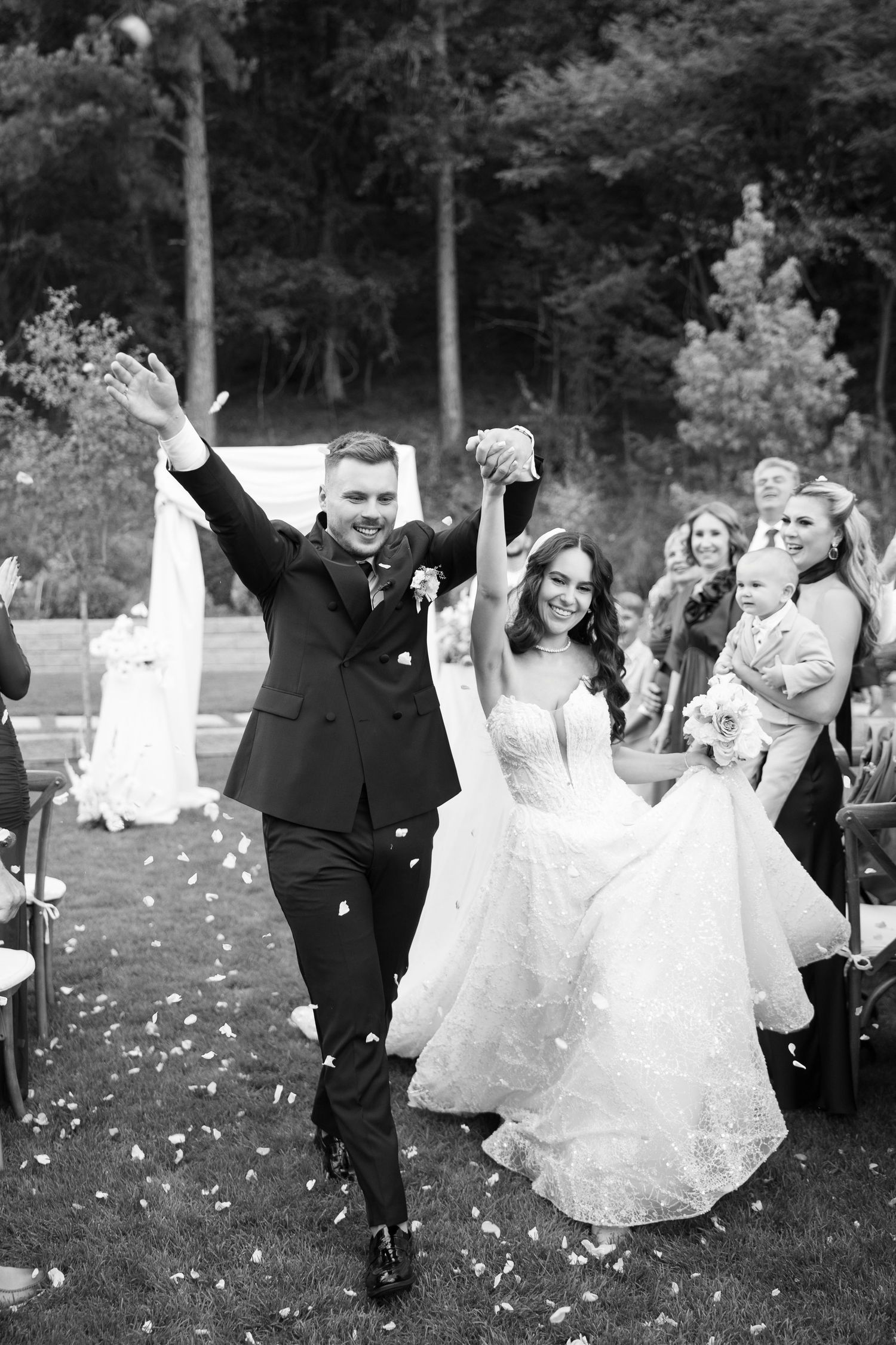 Wedding party celebrates joyfully on a grassy lawn with confetti flying through the air during an outdoor celebration.