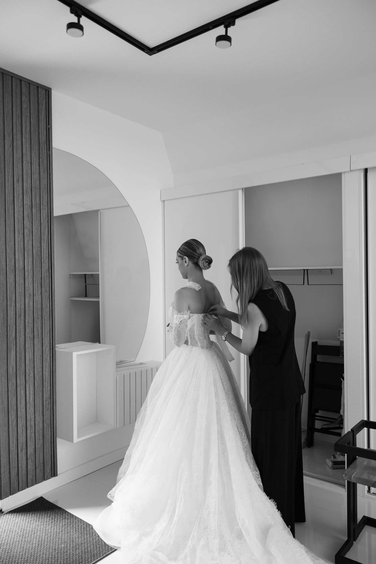 Wedding dress preparations in a minimalist white room with elegant lighting.