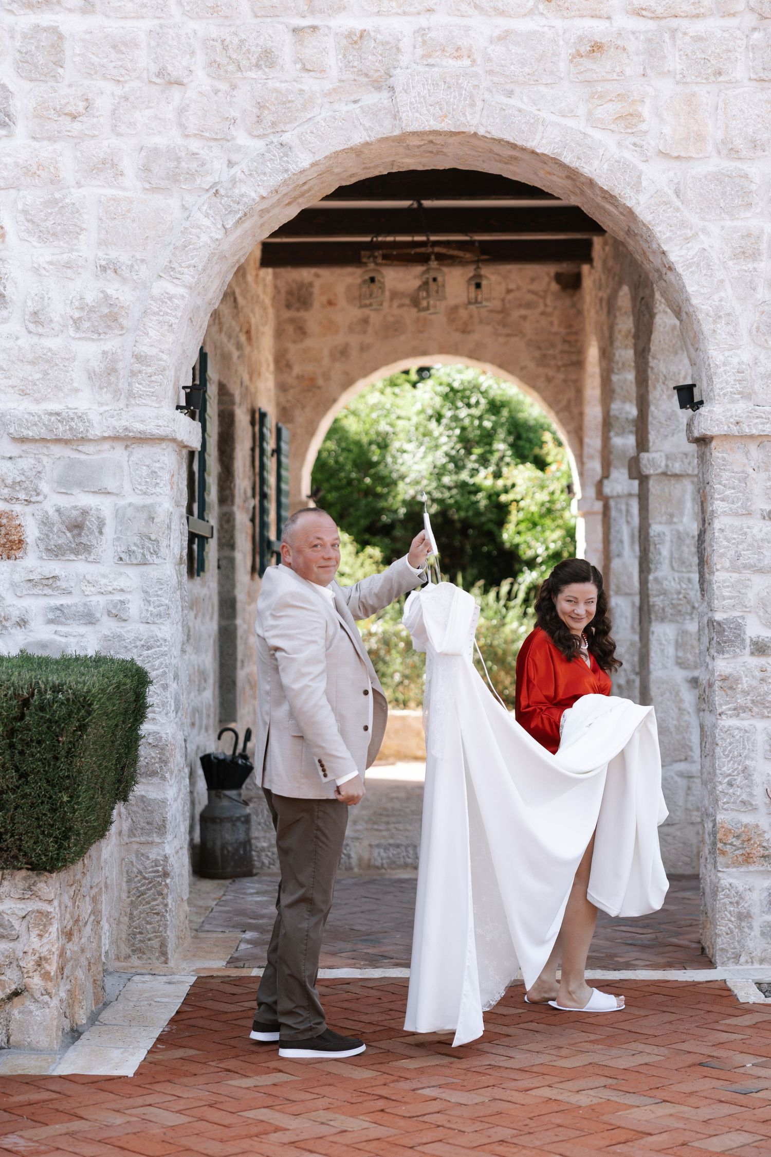 Stone archways with terracotta flooring lead to a garden while decorative white figures line the walkway.
