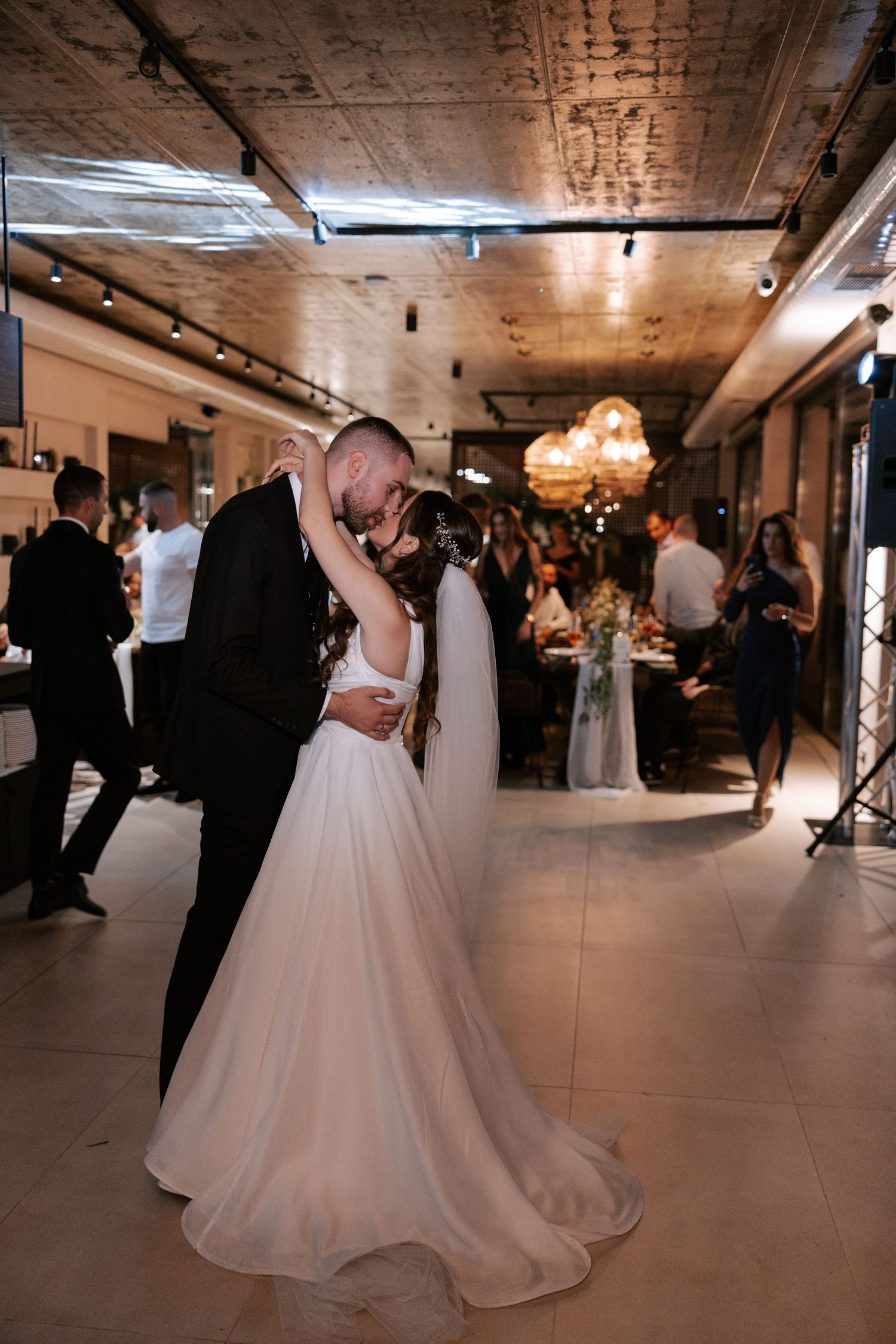 Newlyweds share an intimate dance moment in an industrial-chic reception venue with exposed ceiling.