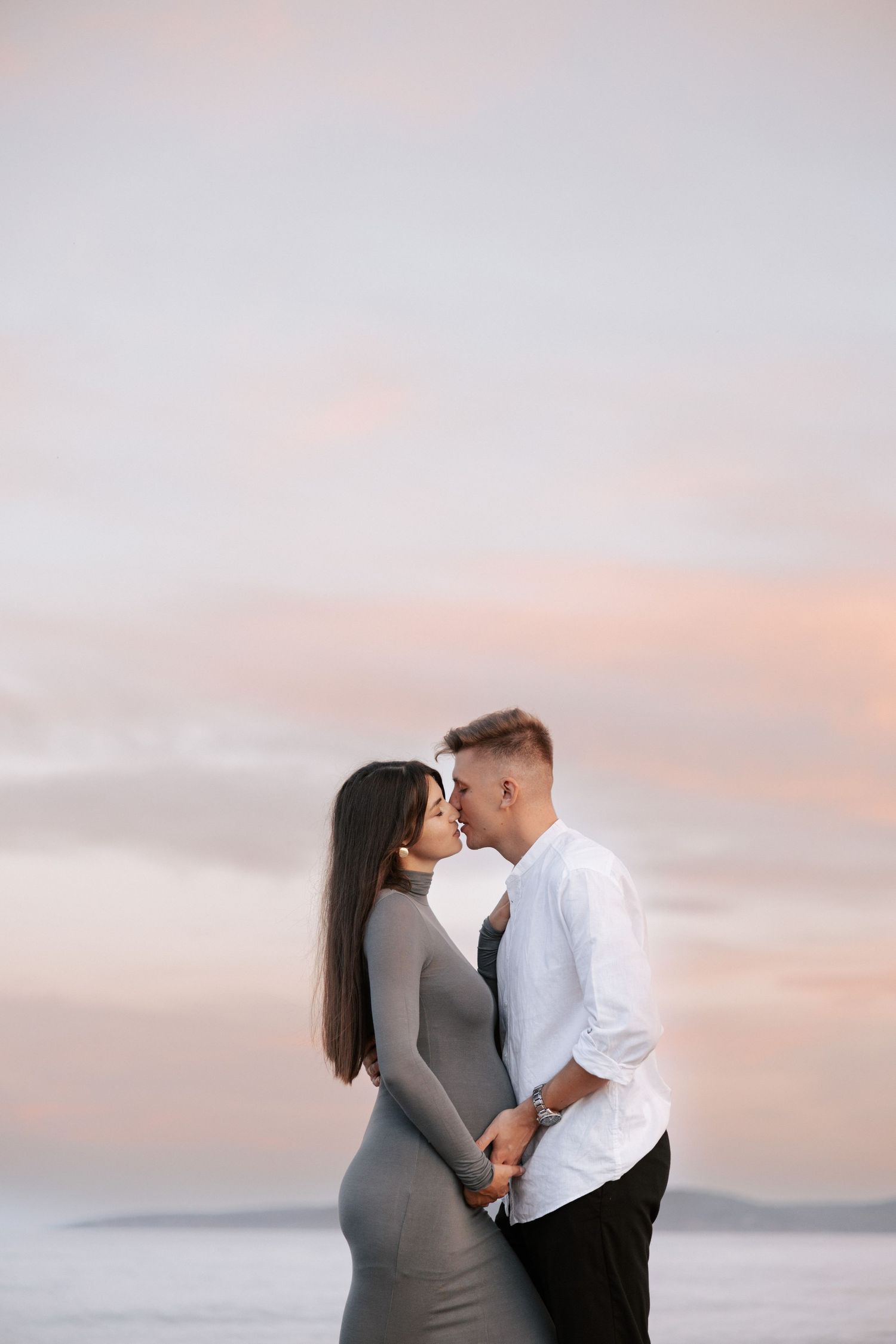 An intimate maternity photo of a couple embracing at sunset by the ocean.