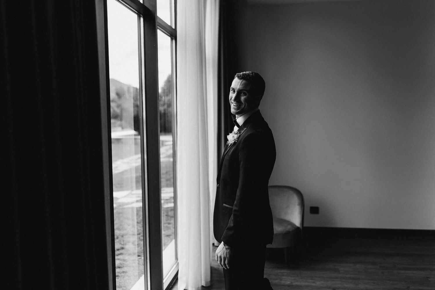 Black and white image of someone in formal wear gazing out a large window.