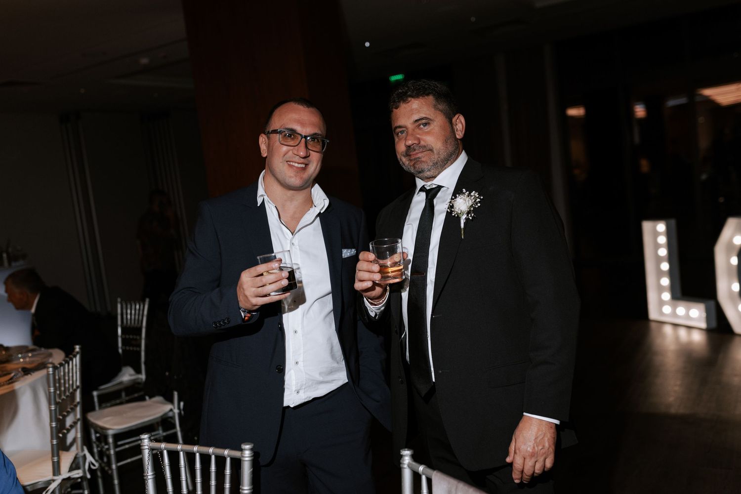Two guests enjoying drinks at an evening wedding reception.
