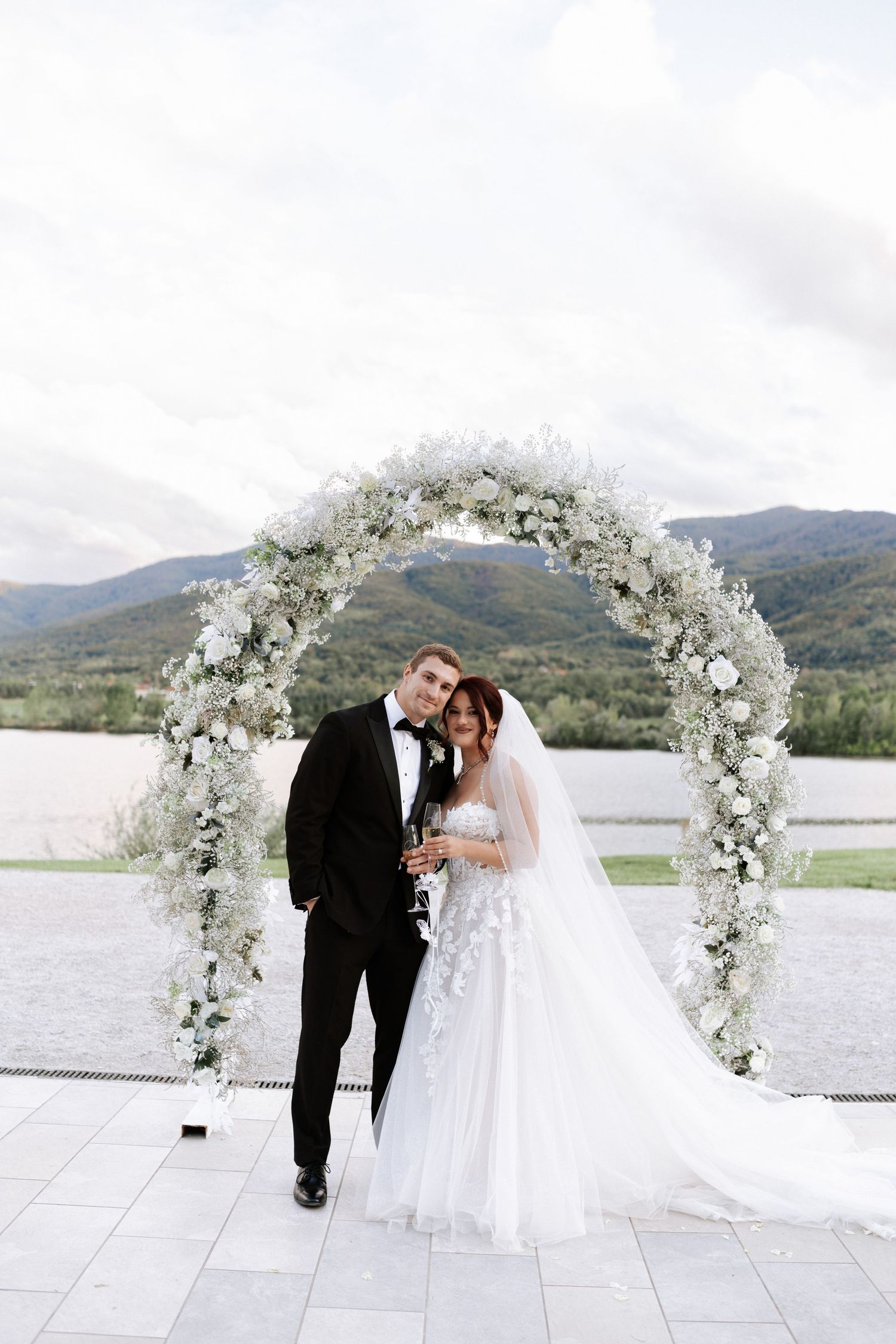 Wedding ceremony setup featuring a luxurious white floral arch against mountainous landscape.