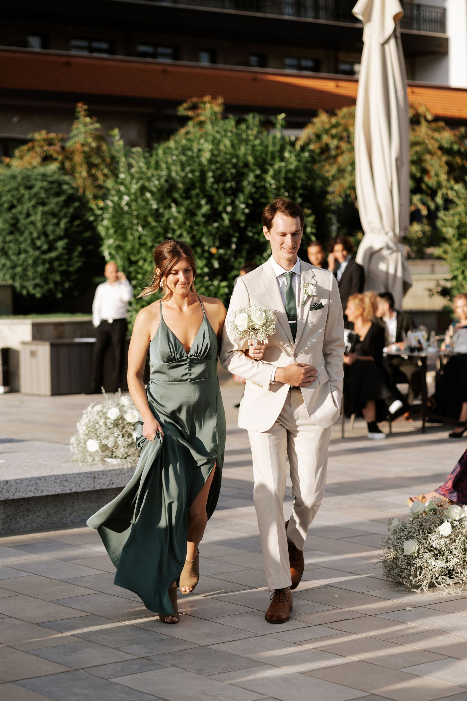 Wedding party members walking across stone patio during outdoor celebration.