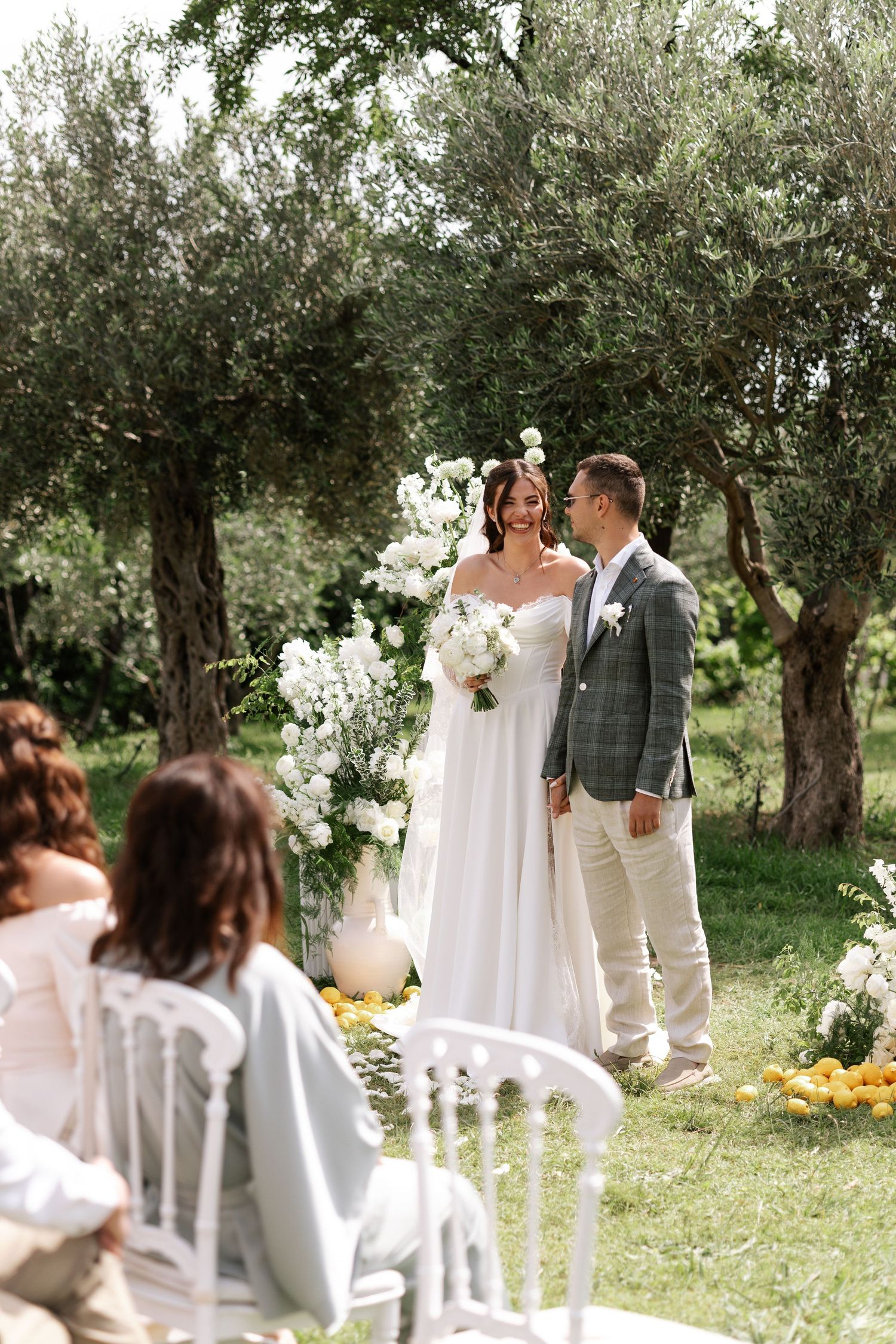 A romantic outdoor wedding ceremony setup in an olive grove with white chairs and floral decorations.