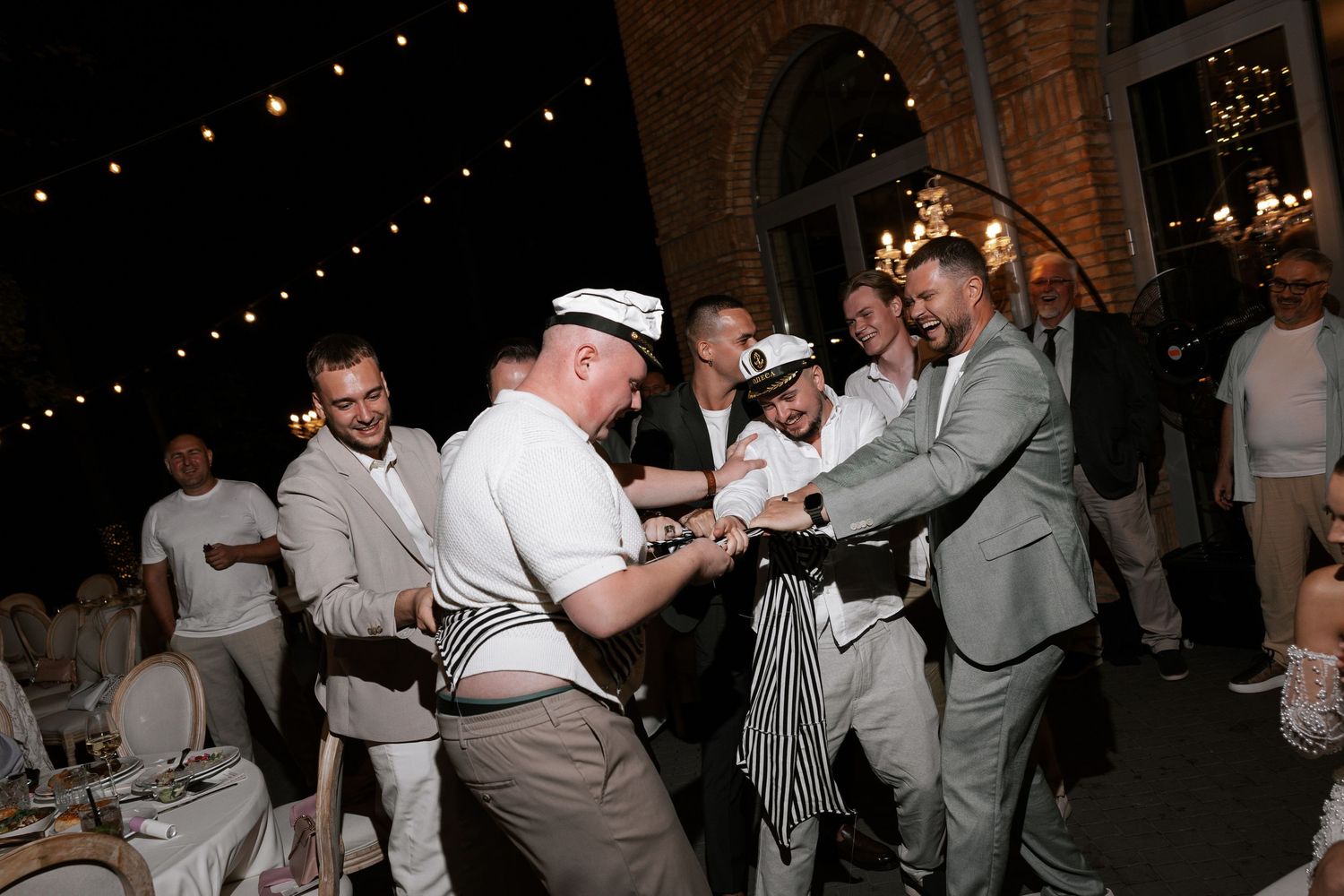 Wedding guests dancing and celebrating in a rustic brick venue with string lights overhead.
