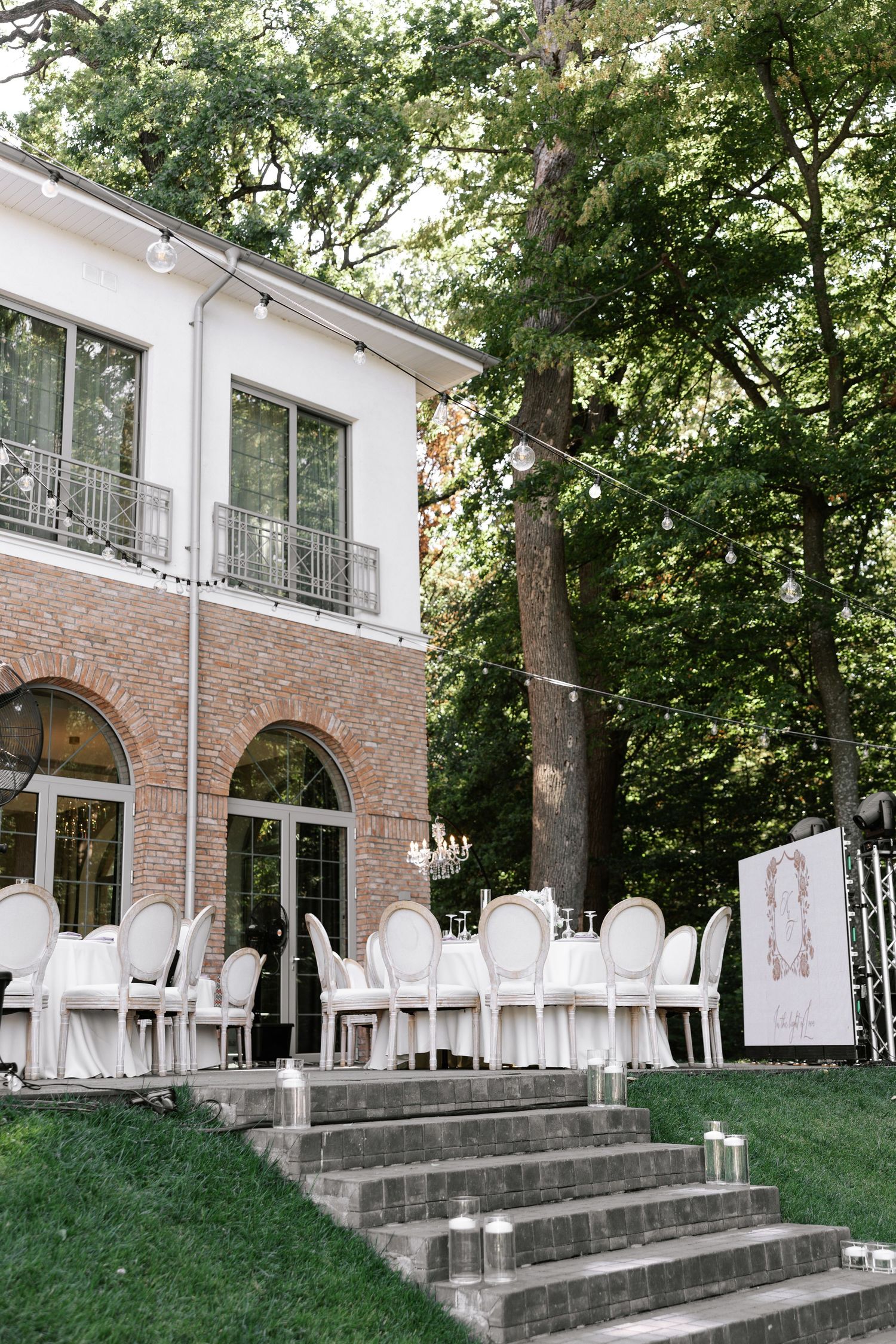 Elegant white chairs are arranged on a grassy lawn in front of a brick building for an outdoor wedding.