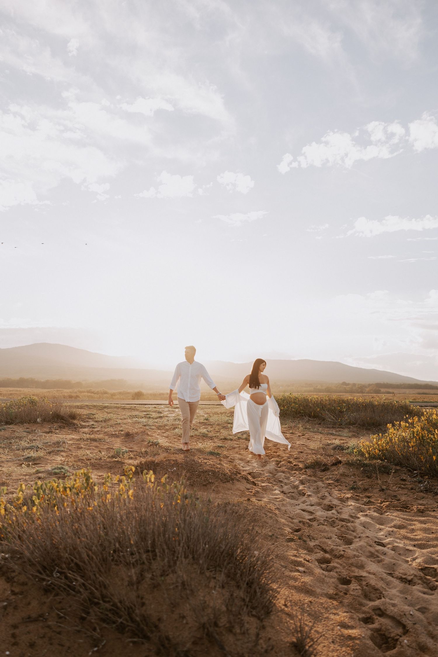 Romantic couple walks hand in hand through desert landscape during golden hour.