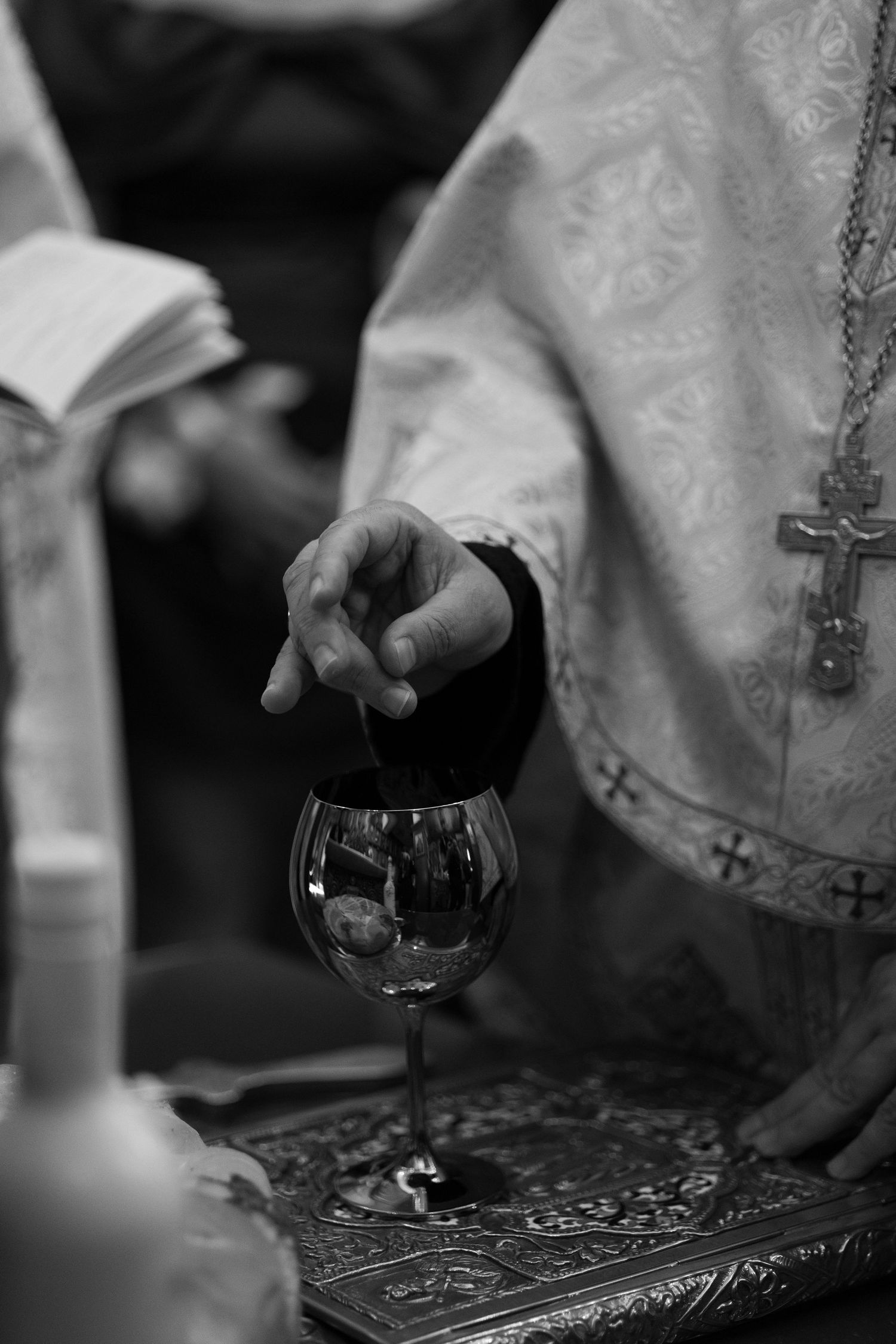 Black and white photo of hands pouring wine into glasses during an Orthodox Christian religious ceremony.
