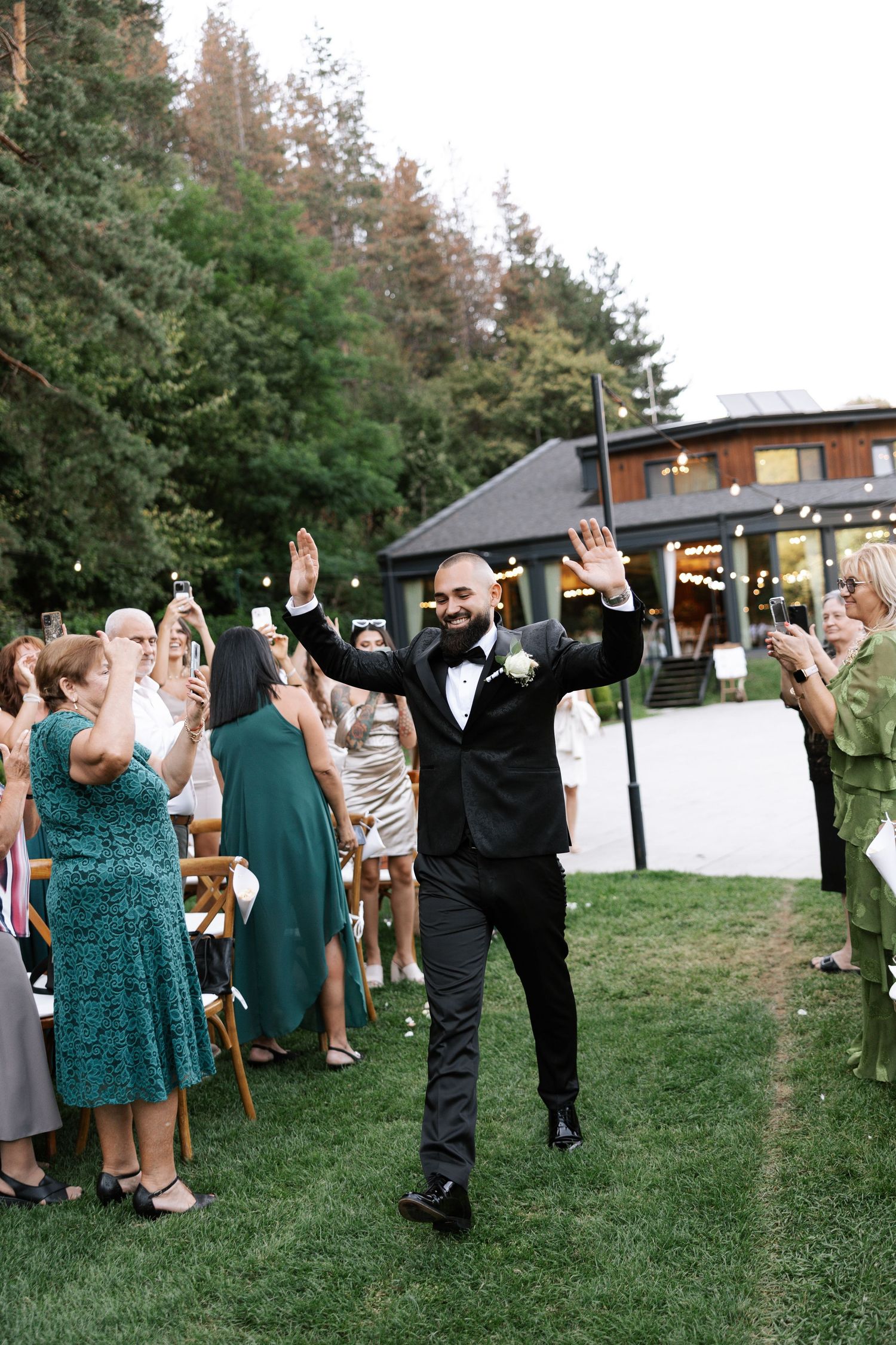 A sequence of candid outdoor party moments showing guests dancing and celebrating on a grassy lawn near wooden buildings.