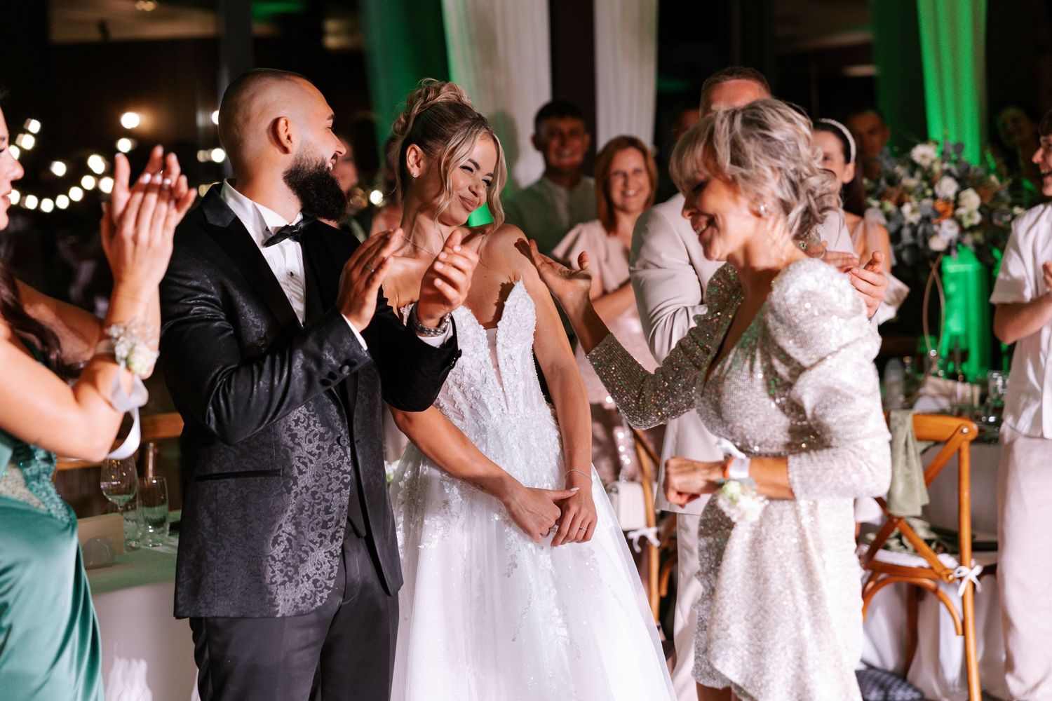 Wedding guests dance together at a reception with green uplighting illuminating the venue's walls.