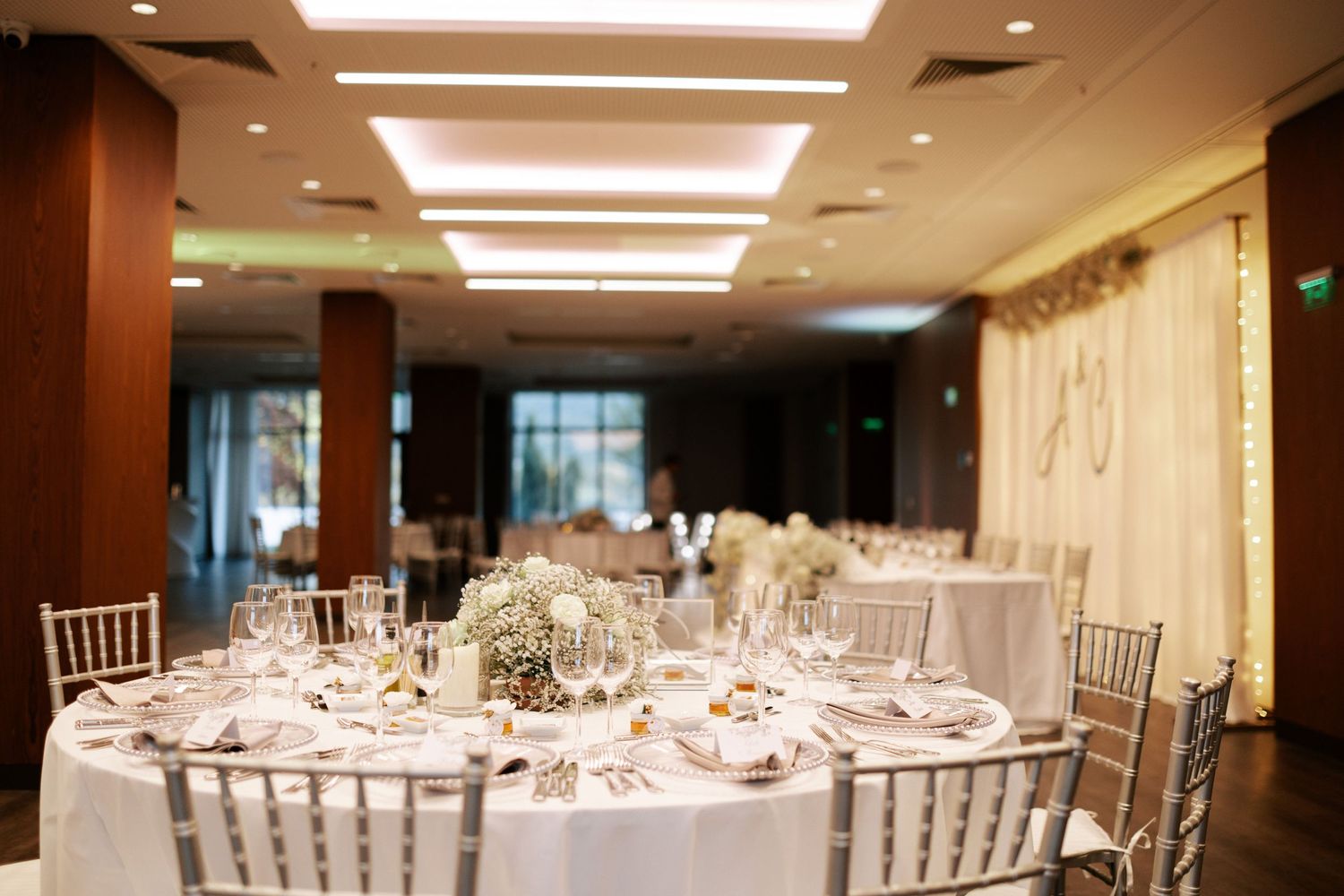 Round tables with white linens and chiavari chairs set up in an elegant ballroom with warm lighting.