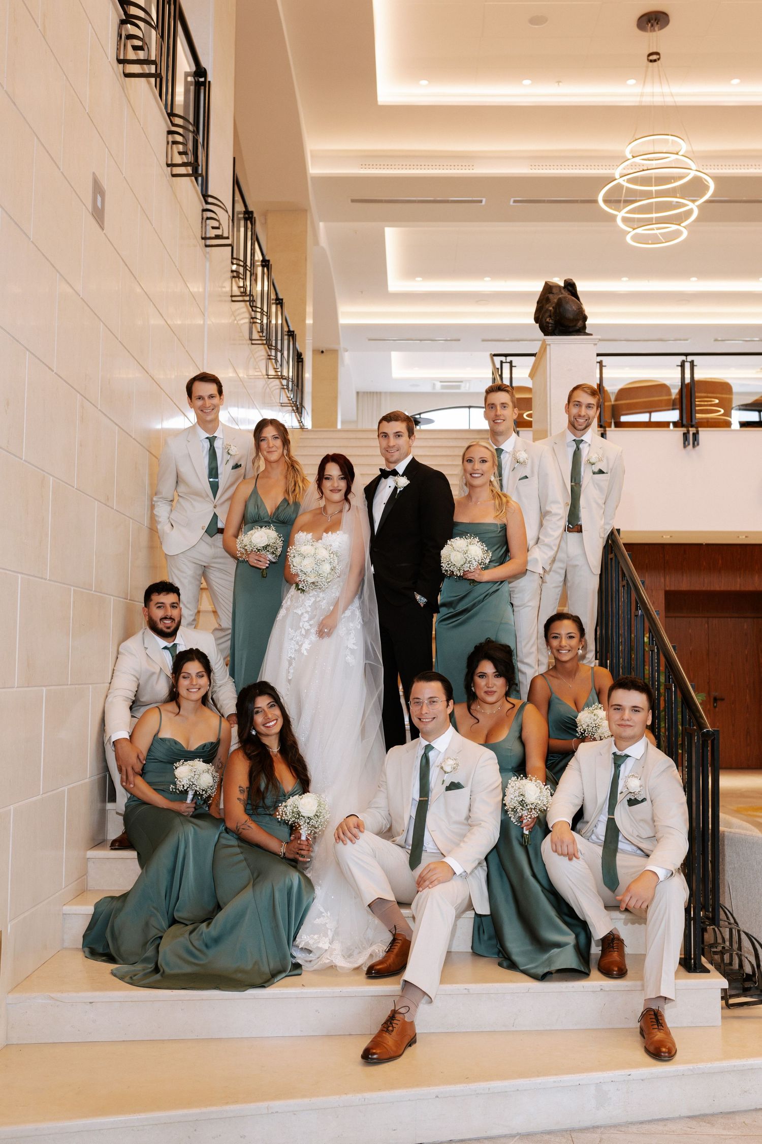 Wedding party poses elegantly on grand interior staircase with modern lighting.