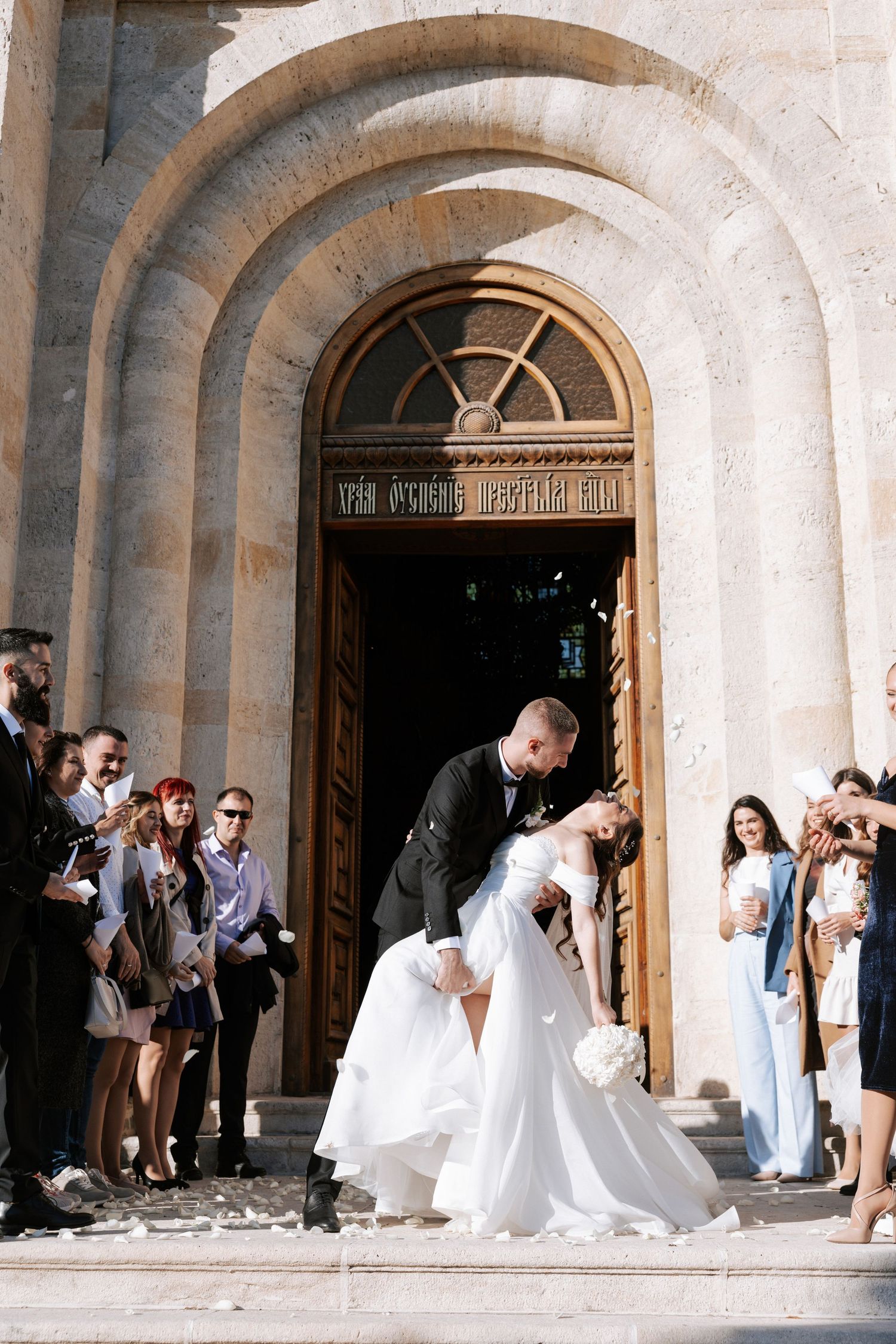 Romantic wedding moment on church steps under arched stone doorway.