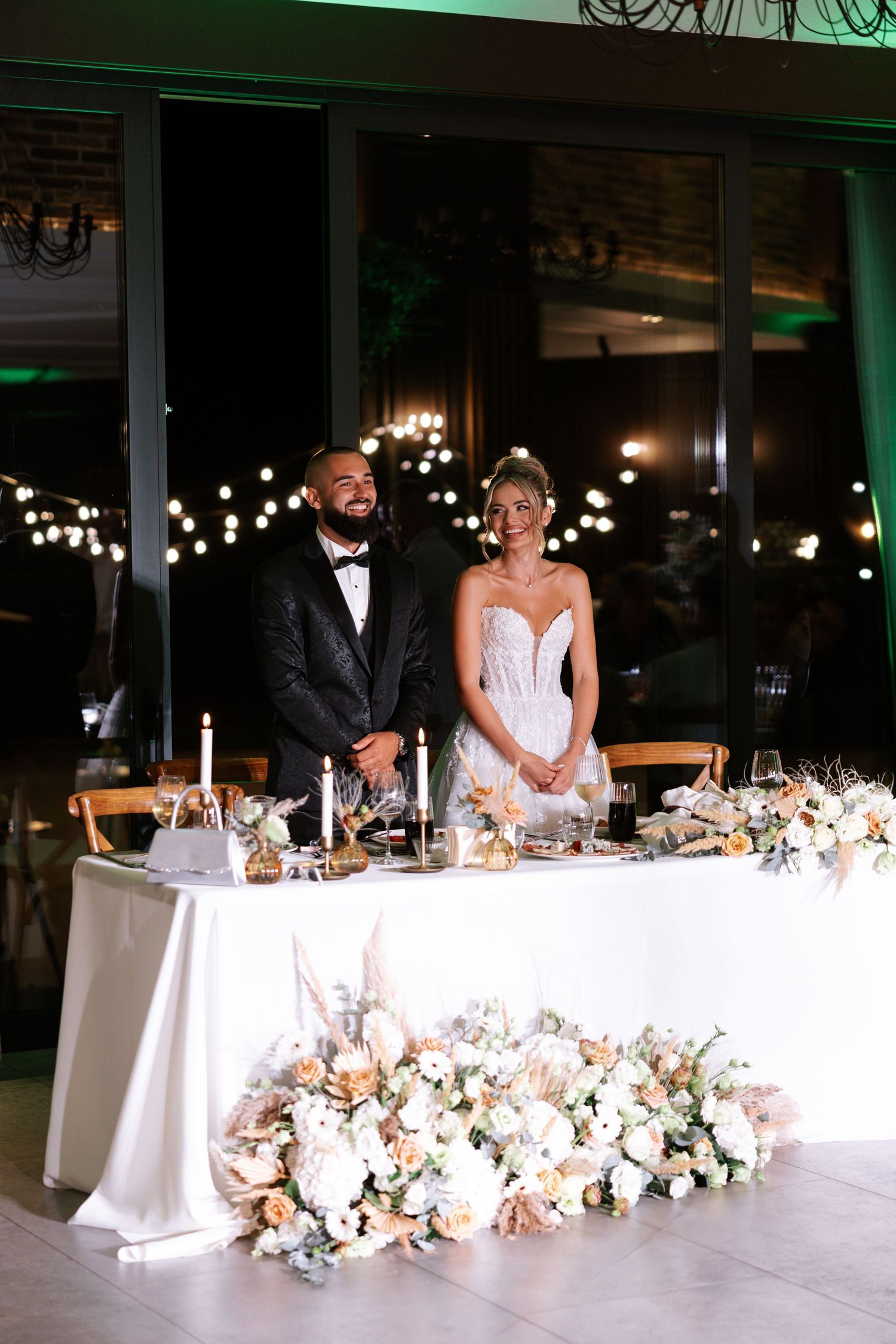 Elegant wedding reception table decorated with lush floral arrangements and white linens at an indoor venue.