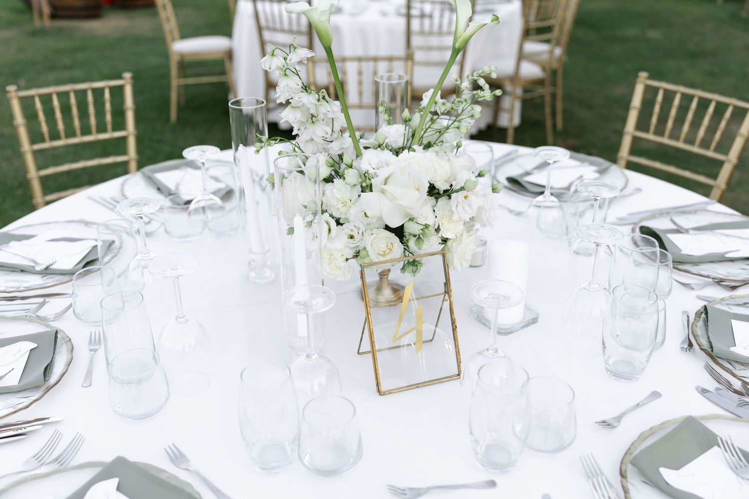 White and gold wedding table settings with crystal glassware and fresh floral arrangements at an outdoor venue.