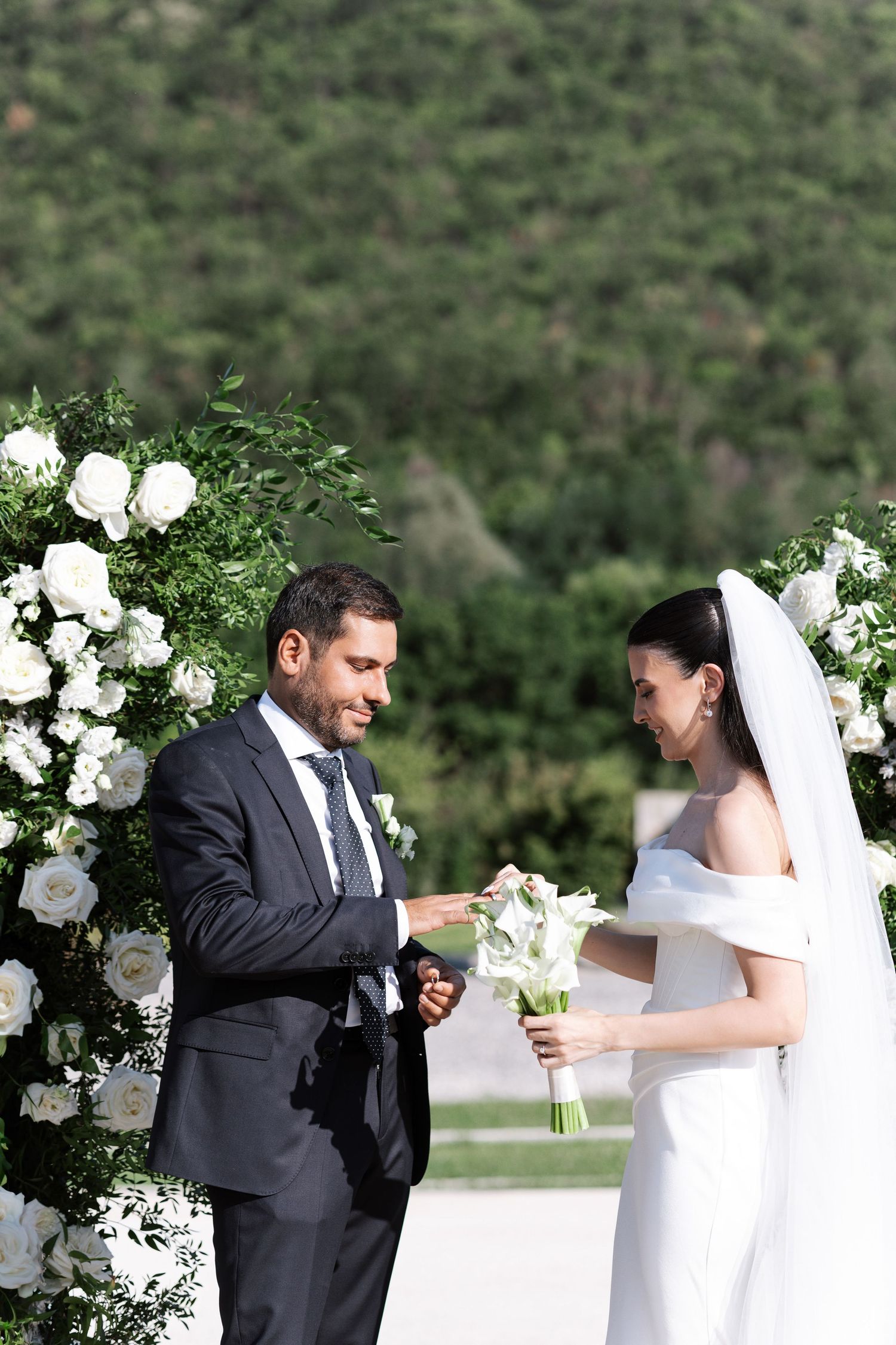A couple shares a playful moment during their outdoor wedding ceremony with white floral decorations.