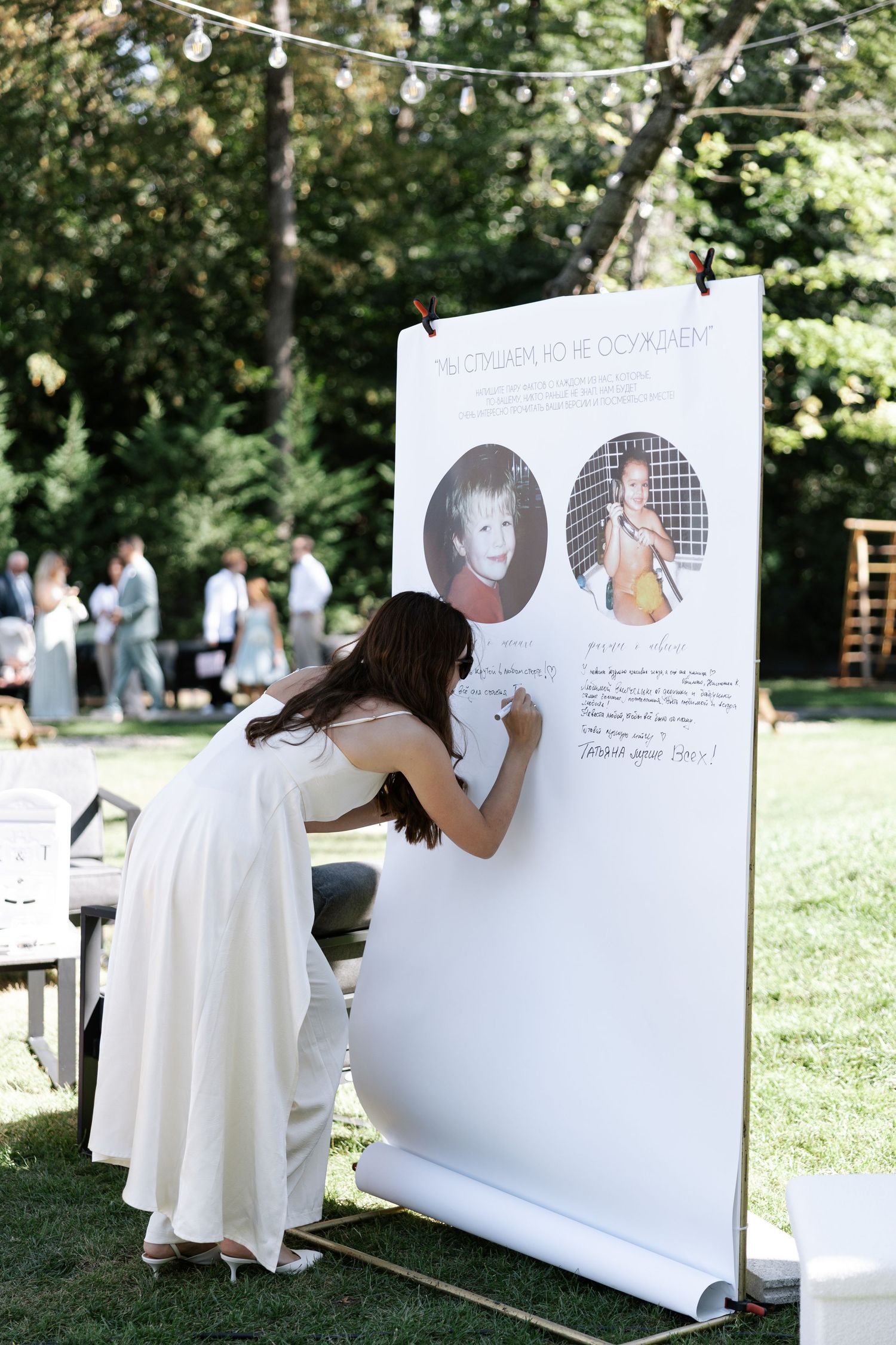 Guests sign a large white display board at an outdoor wedding event.