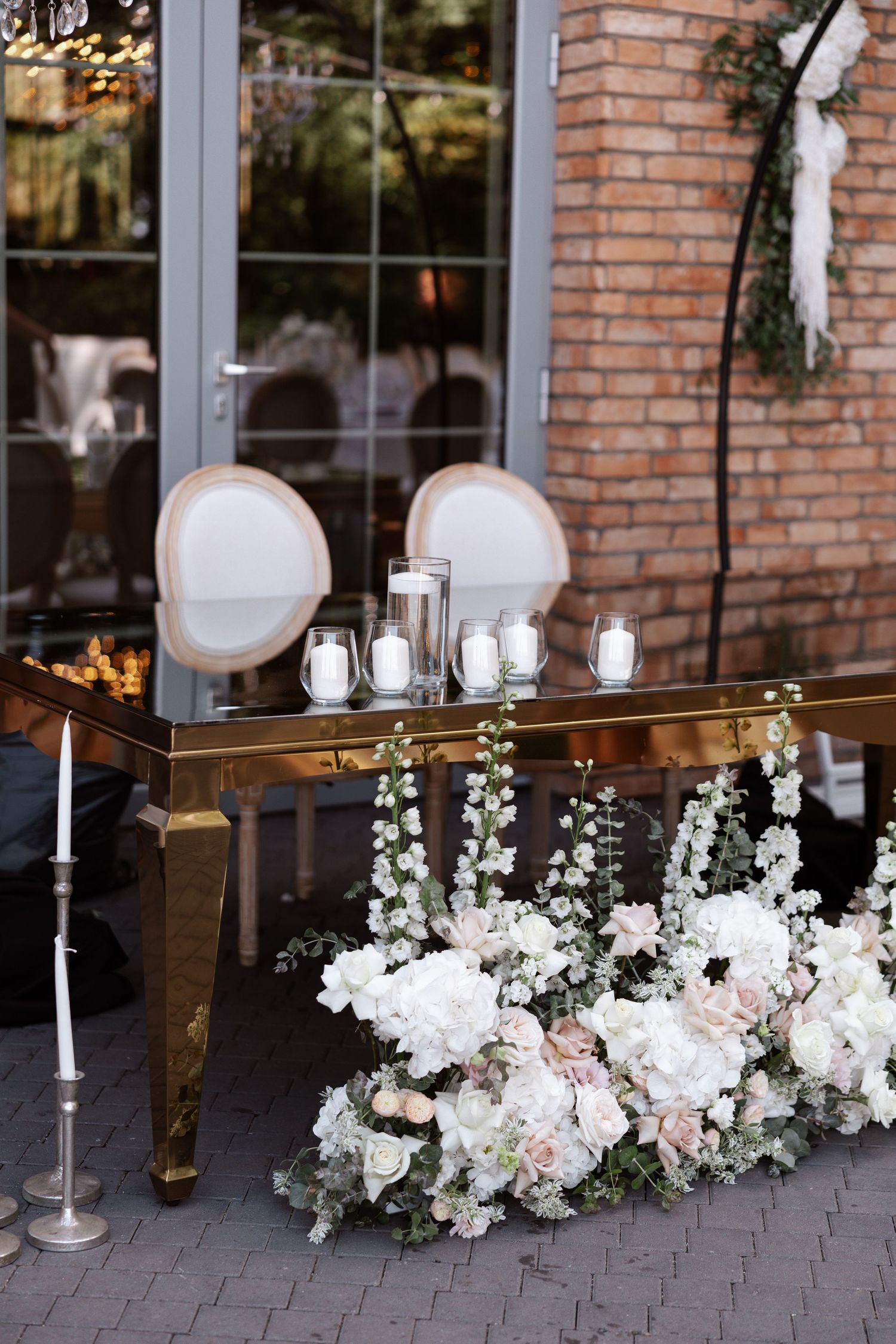Luxurious white floral arrangements with roses decorating a head table at a wedding reception.