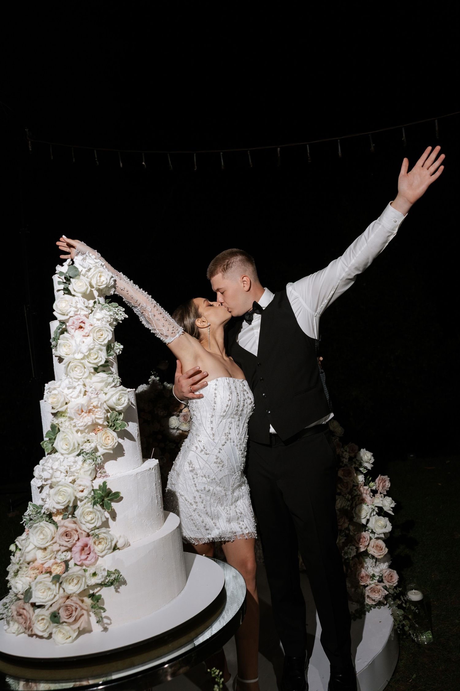 Wedding couple cutting their elegant white tiered cake decorated with fresh flowers.