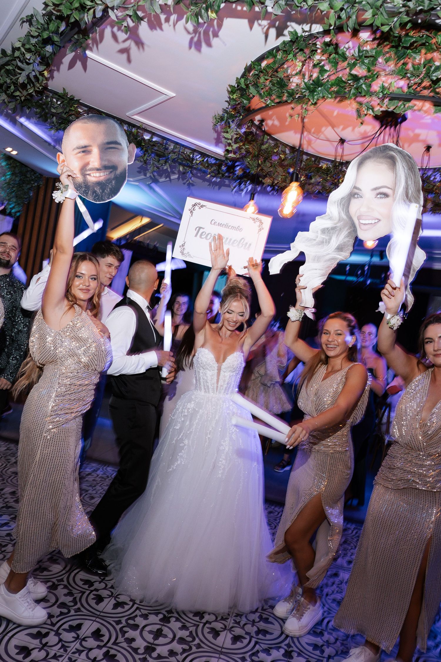 Wedding reception dance floor with guests celebrating under purple lighting and floral decorations.