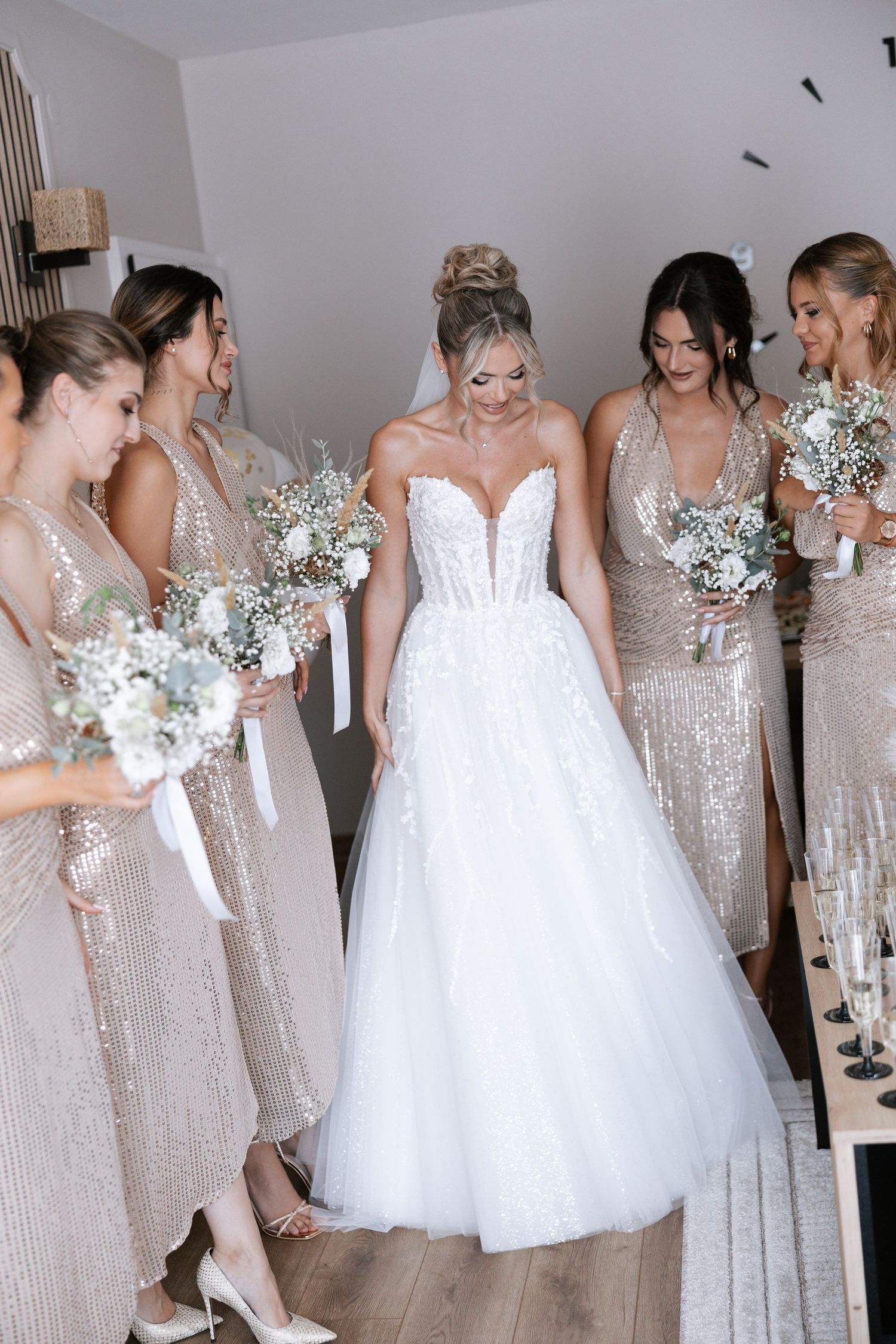 Wedding party in sparkly champagne bridesmaid dresses and white bridal gowns gathered in a candid moment.