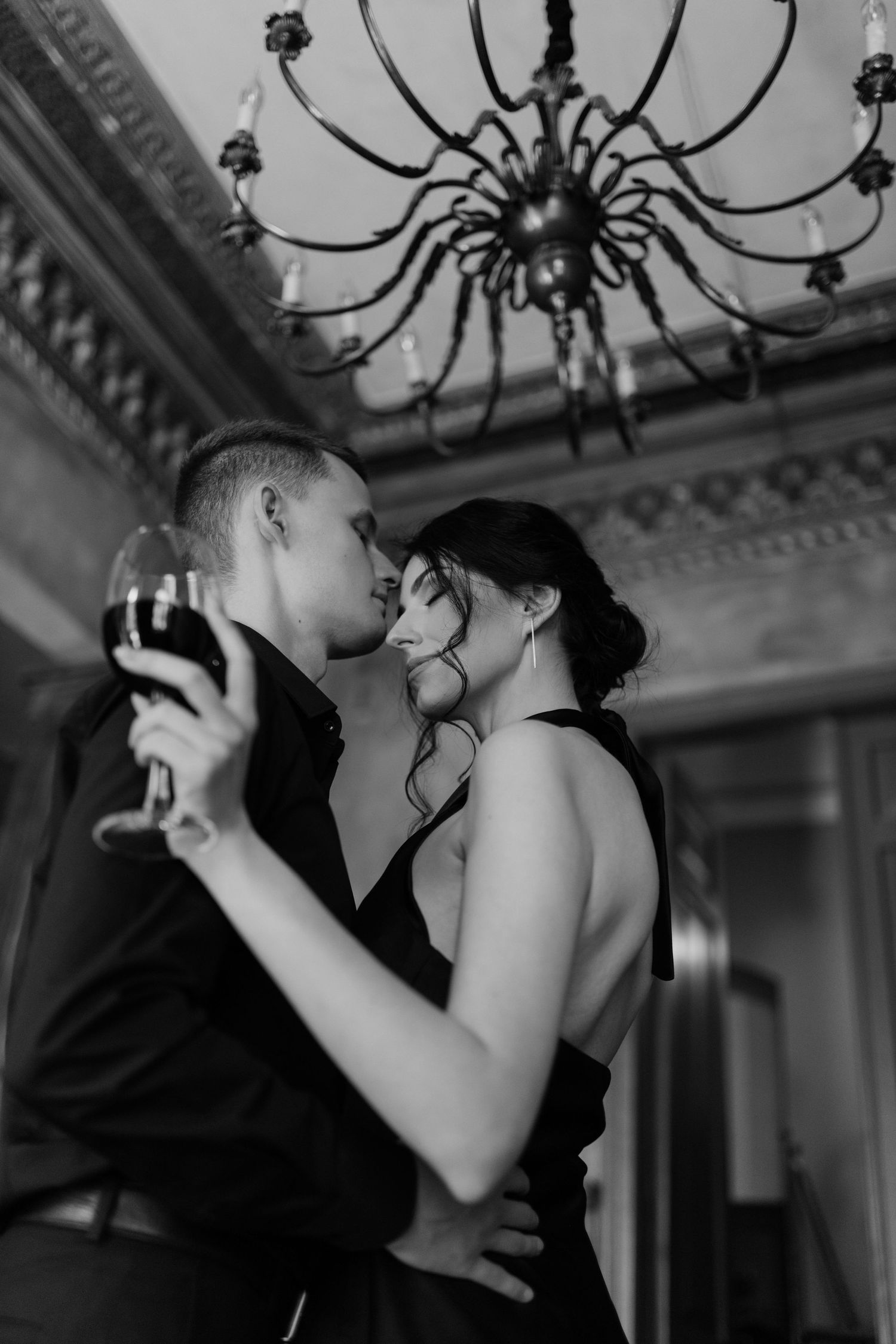 Romantic black and white photo of couple dancing beneath vintage chandelier.
