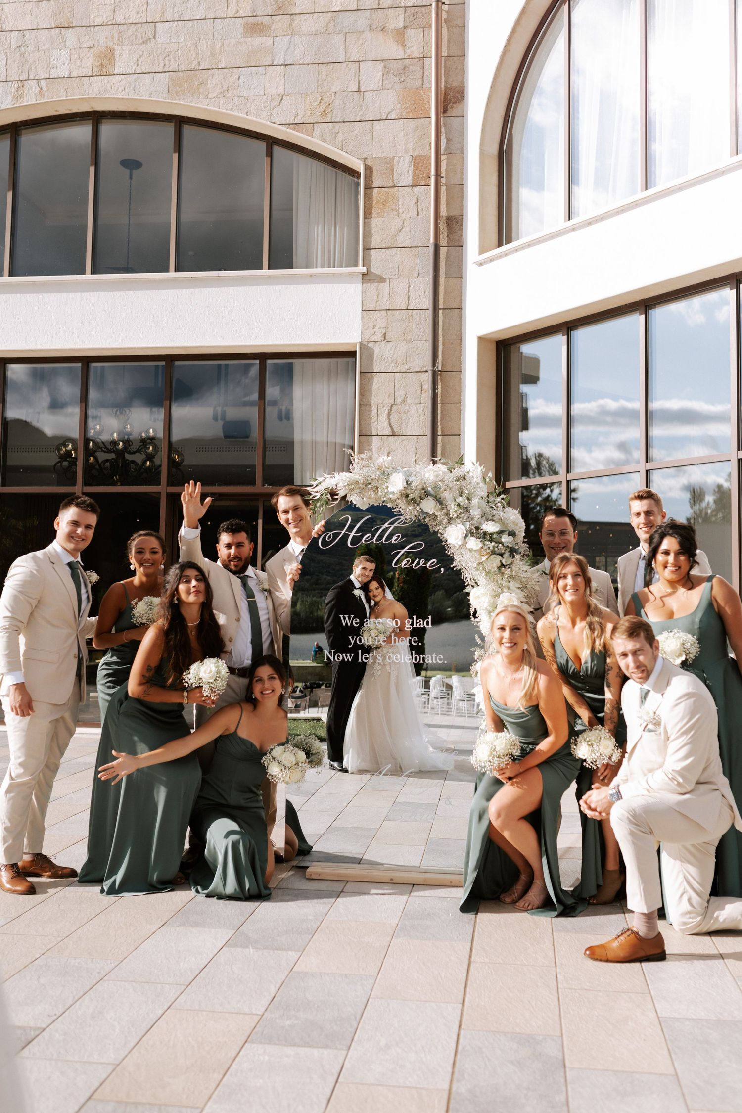 Wedding party poses casually outside modern building with stone facade.