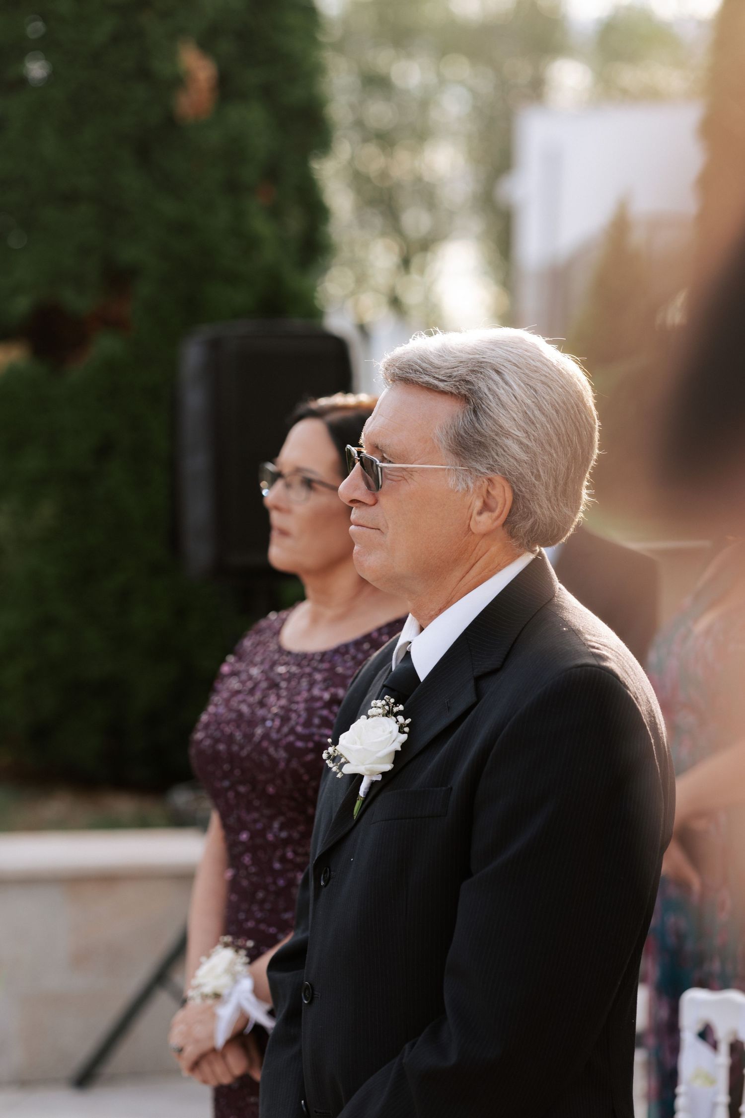 Wedding guests in formal attire watch the ceremony during golden hour.