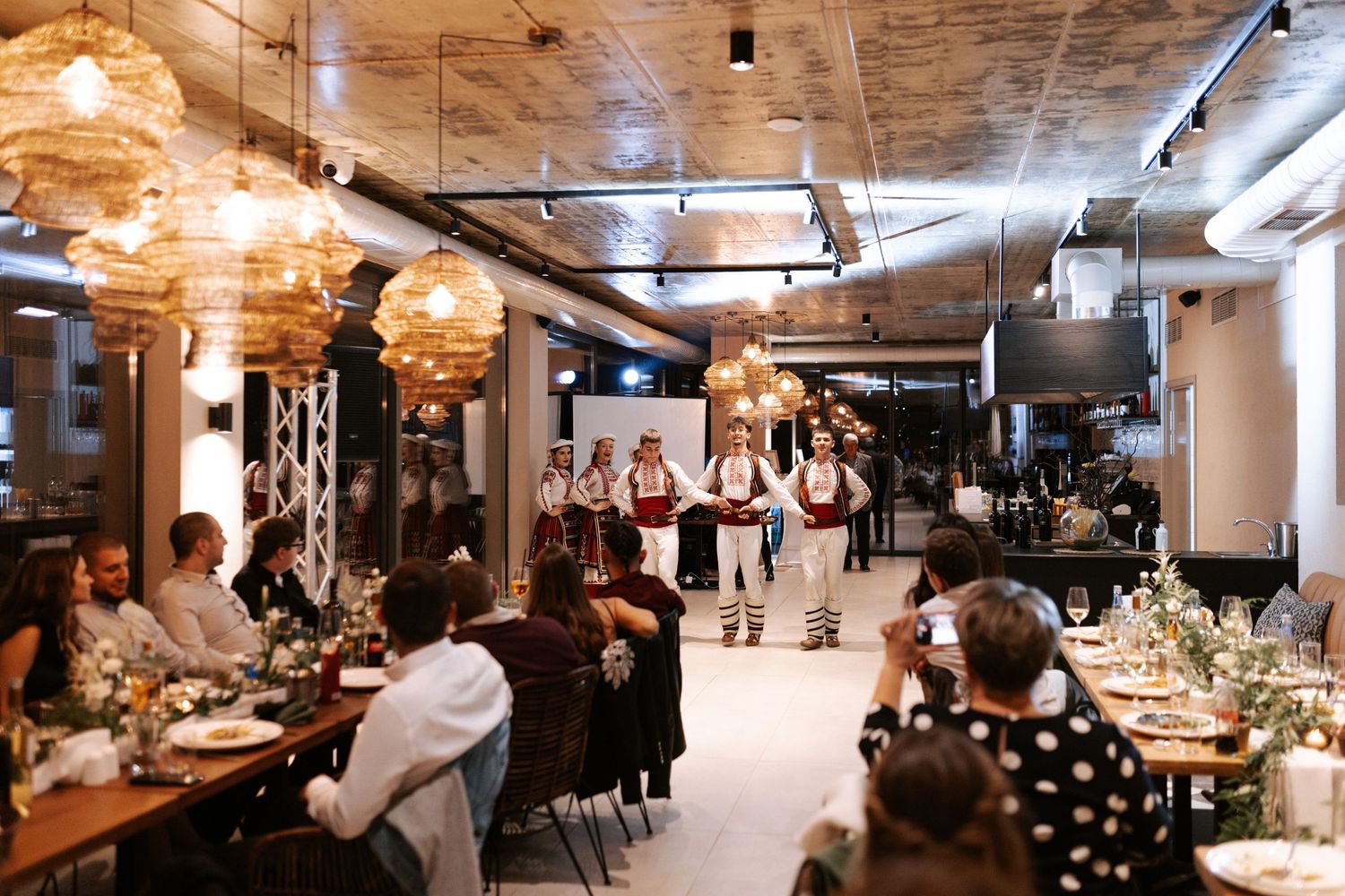 Modern restaurant interior with pendant lighting and guests seated at long tables during an event.