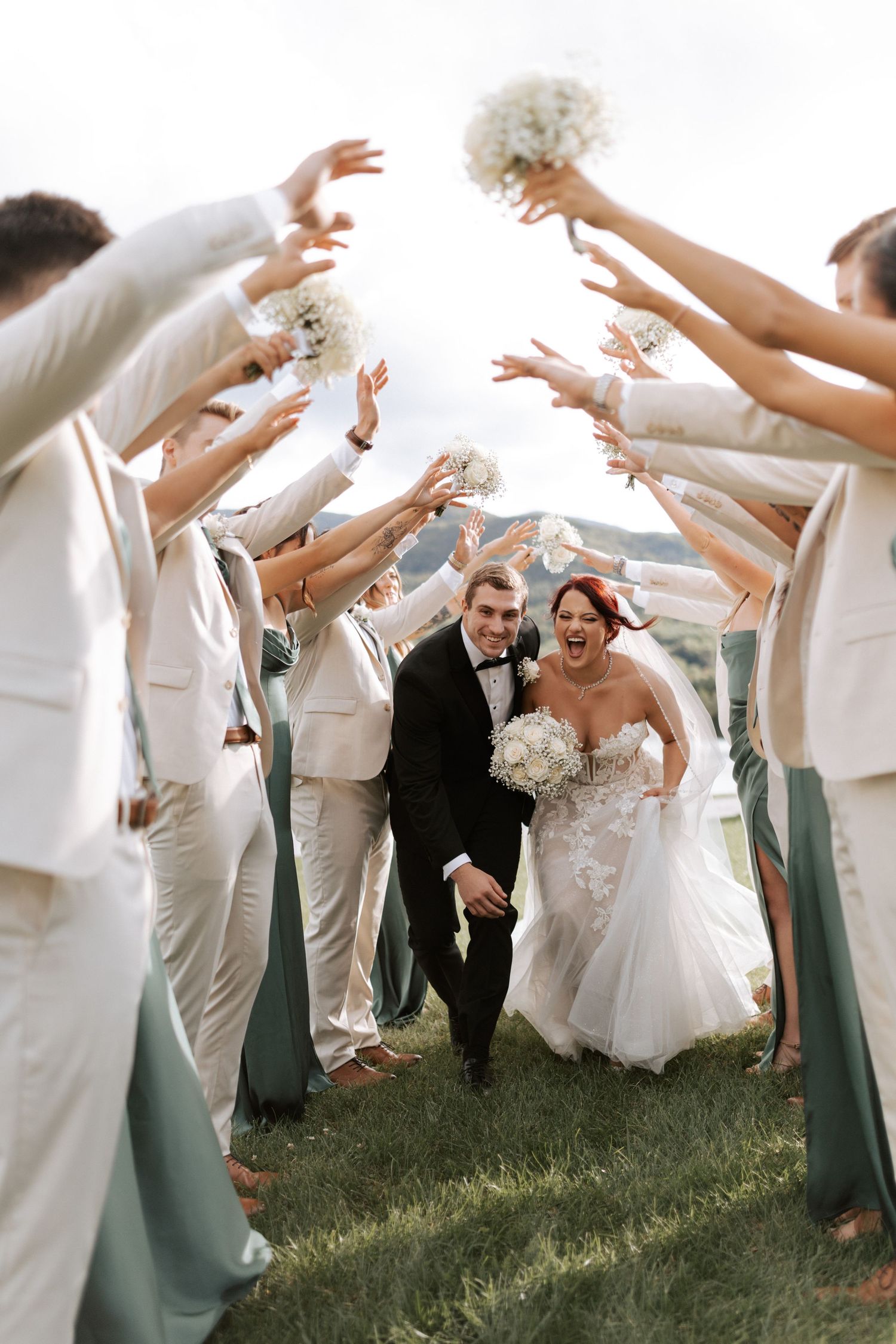 Wedding party forms a tunnel with raised arms holding bouquets under cloudy skies.Wedding photographer Bulgaria