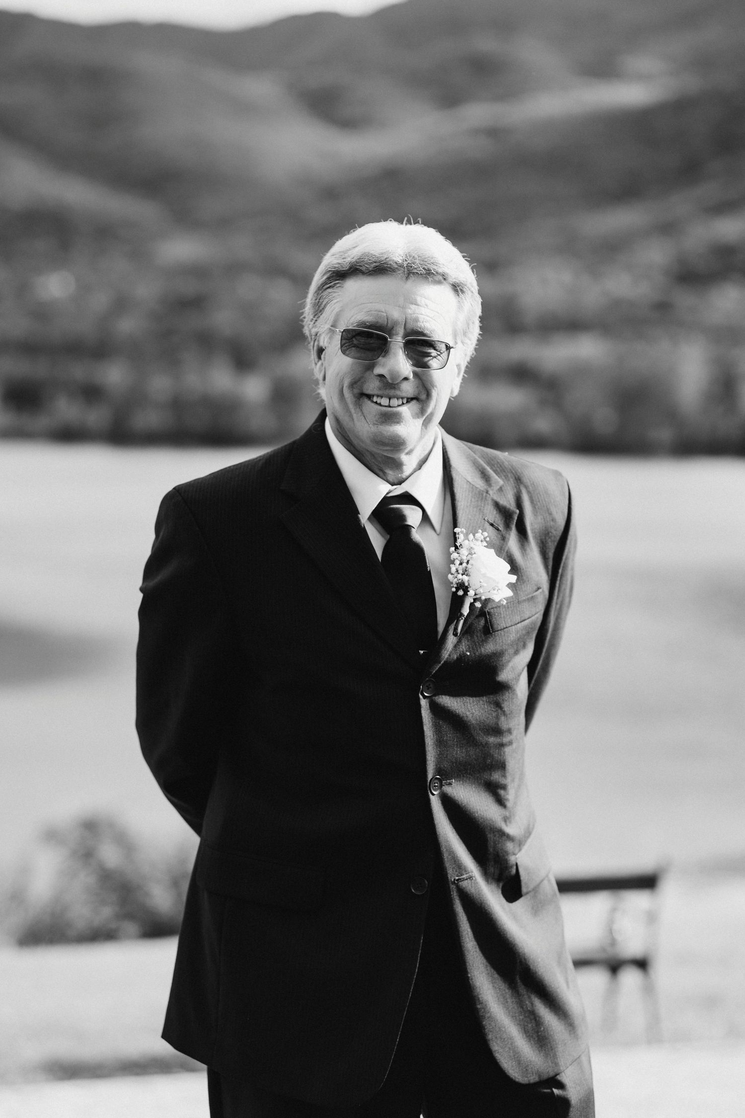 Black and white portrait of a distinguished gentleman in a suit with mountain scenery behind.
