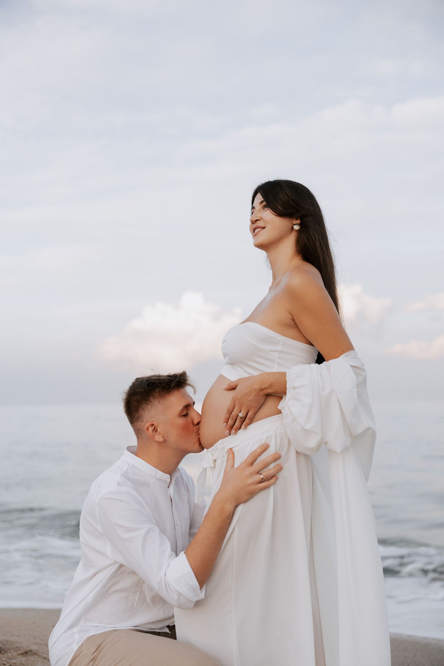 A tender moment between expecting parents during a beach maternity photoshoot.