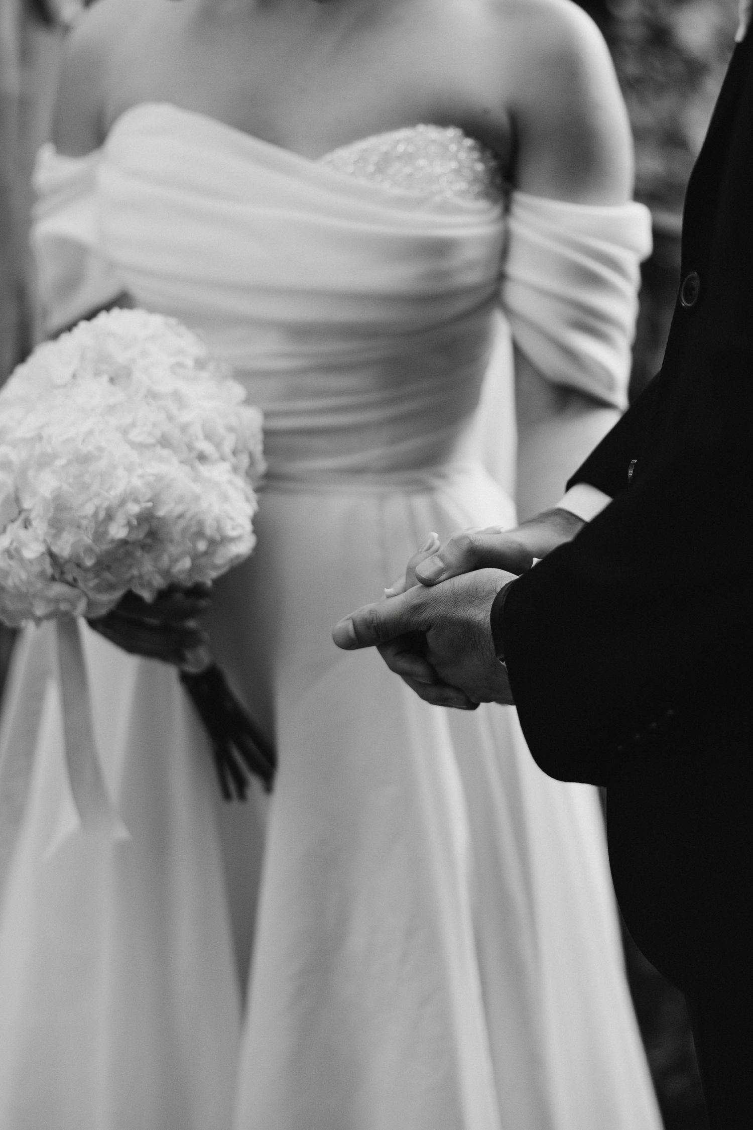 Close-up of wedding attire showing a white dress and hands during ceremony.