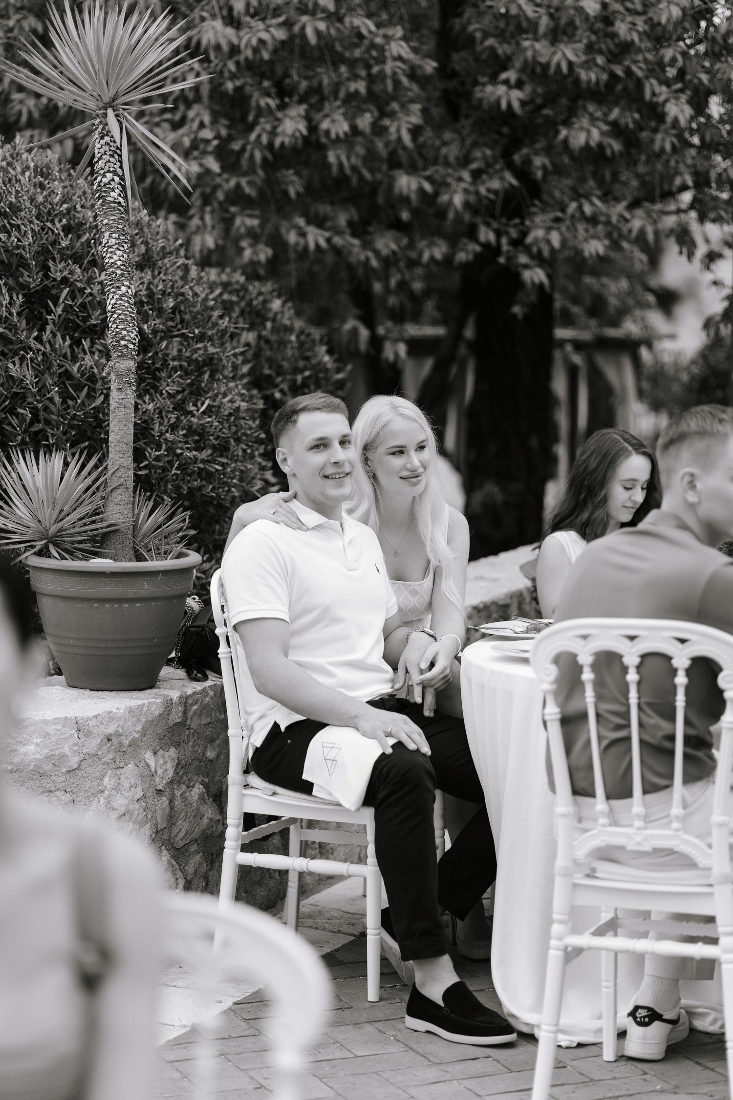 A romantic black and white photo series showing tender moments between a couple sitting on white garden chairs.