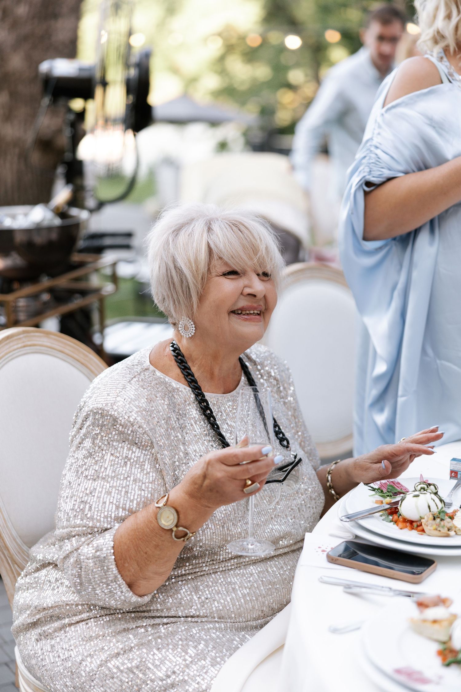 Guest in a sparkly silver dress enjoying dinner at an outdoor wedding reception.
