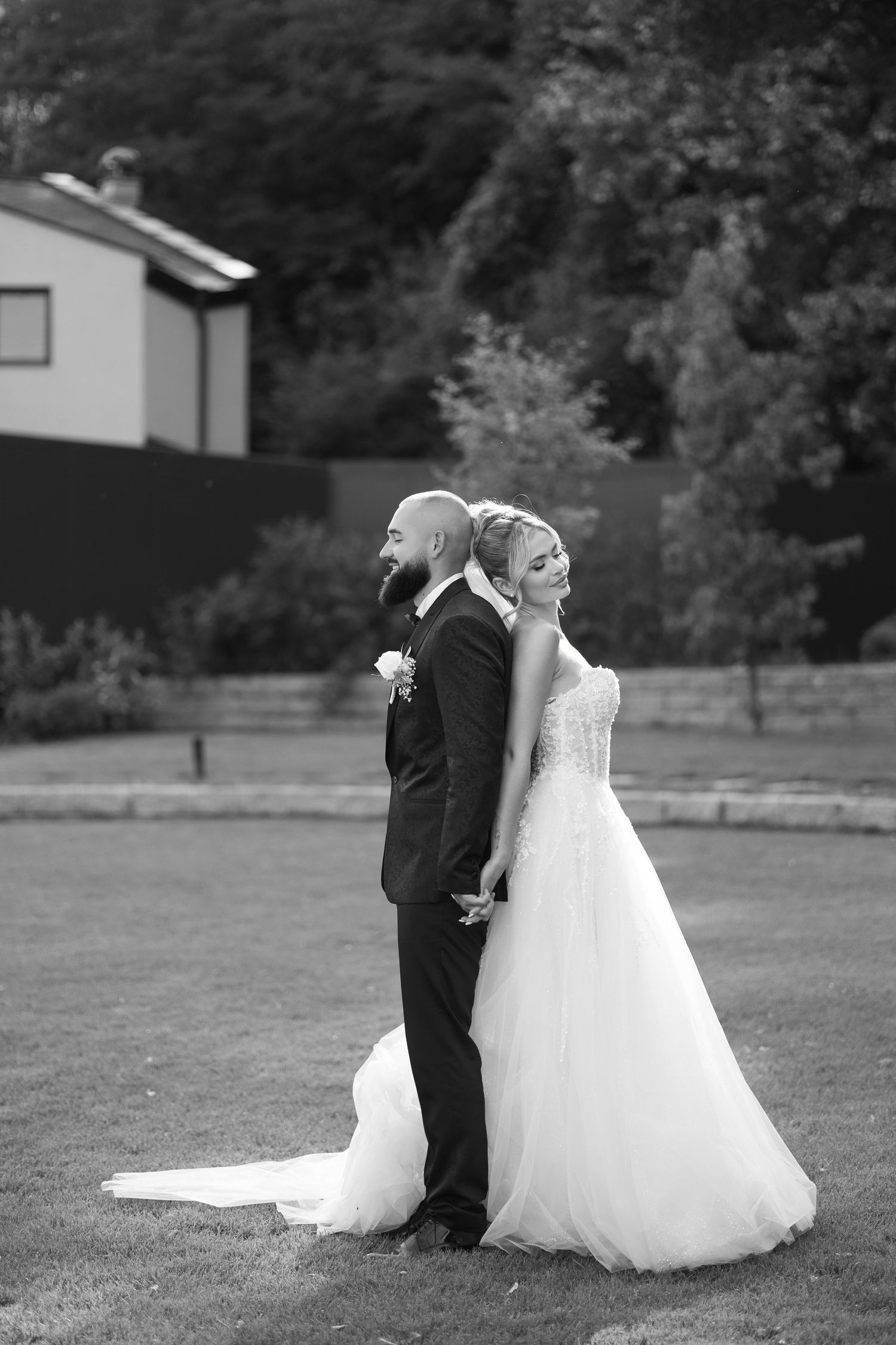 A romantic black and white wedding photo series showing a couple in formal attire embracing outdoors in a garden setting.