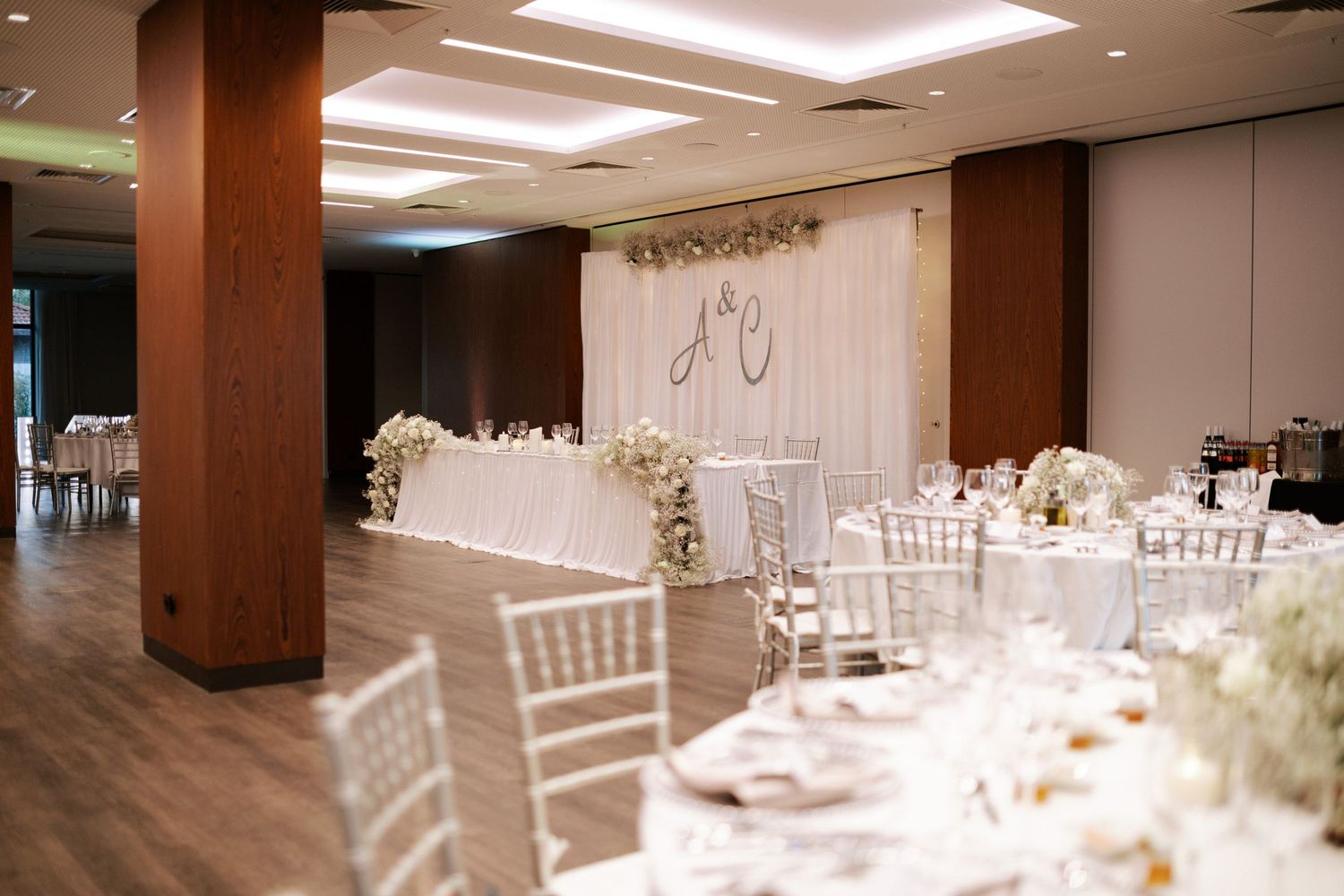 Modern wedding reception venue with white draping, brown columns, and elegant table settings.
