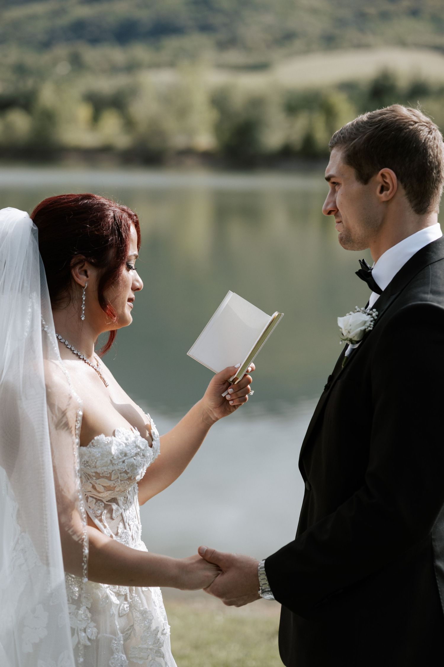 A touching moment during the exchange of personal wedding vows beside a peaceful lake.