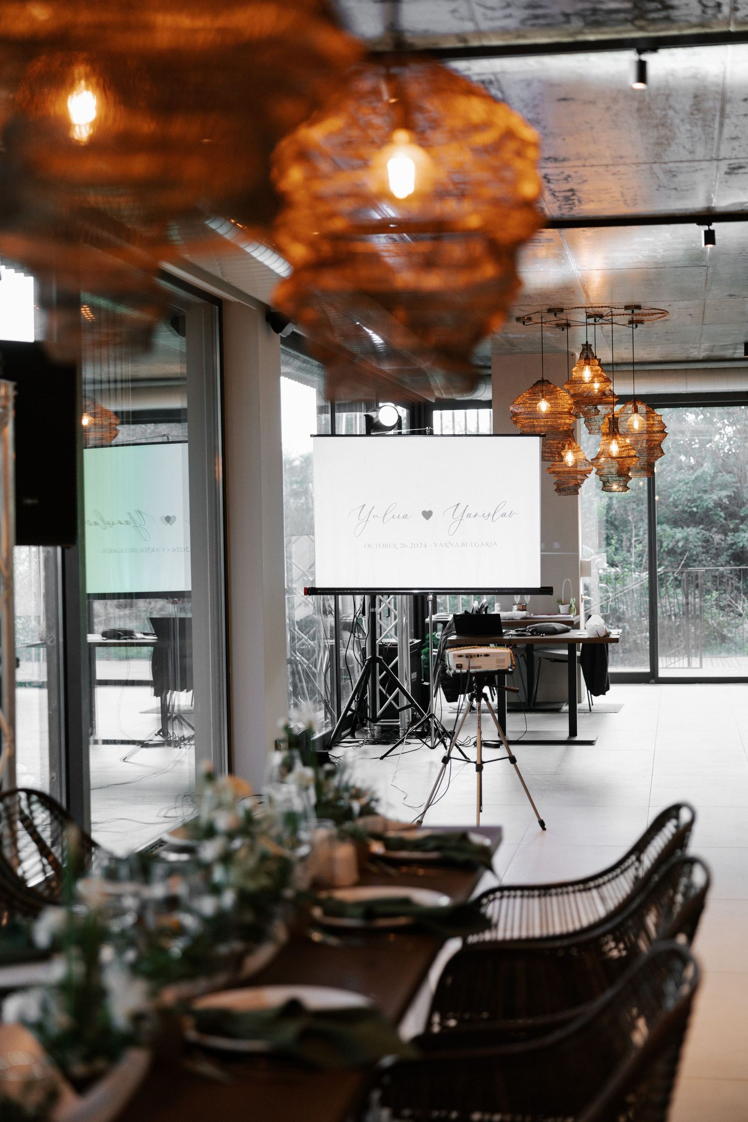 Restaurant interior with woven pendant lights and table settings featuring natural greenery.