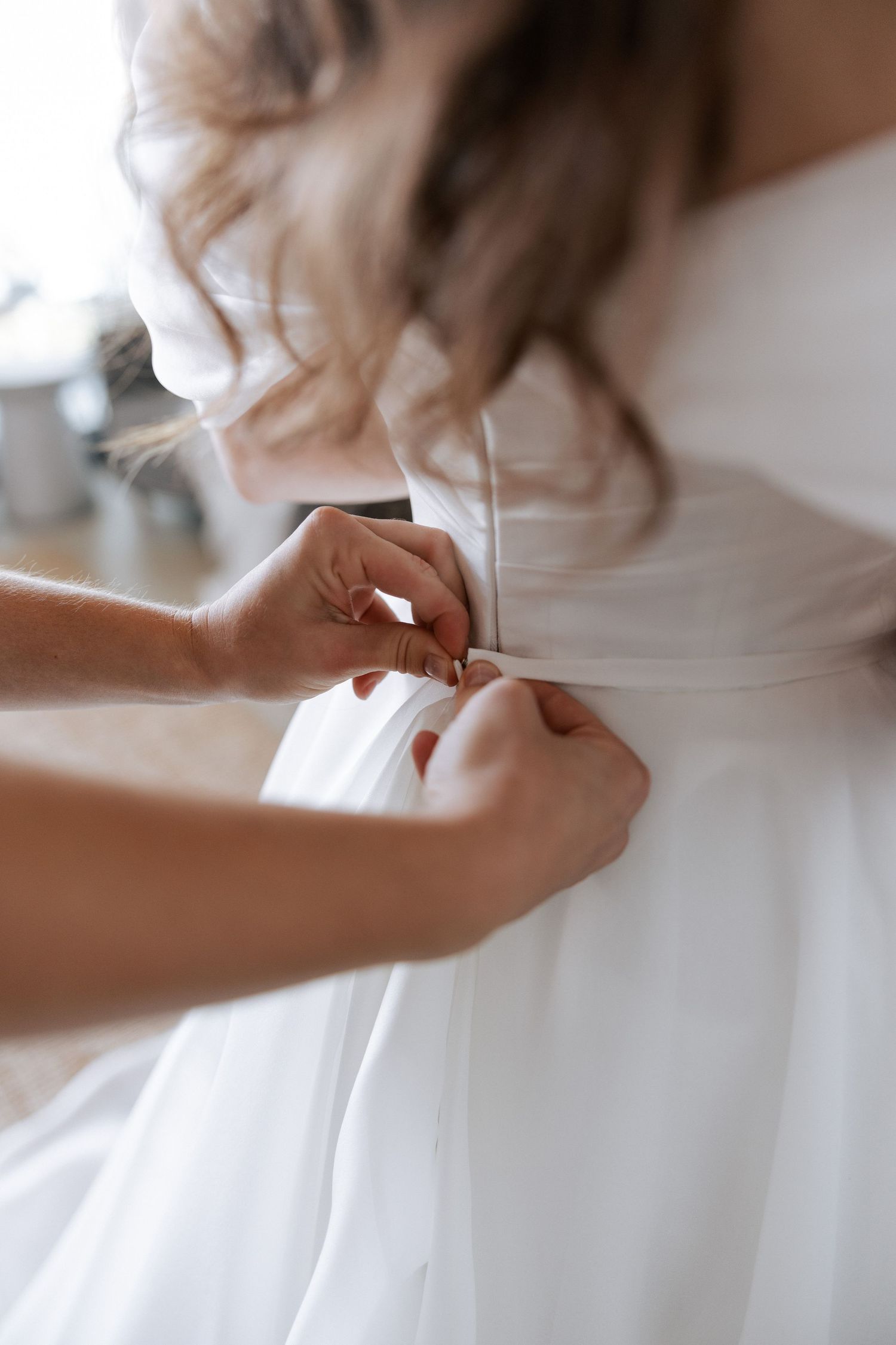 Close-up shot of hands adjusting details on a white wedding dress.