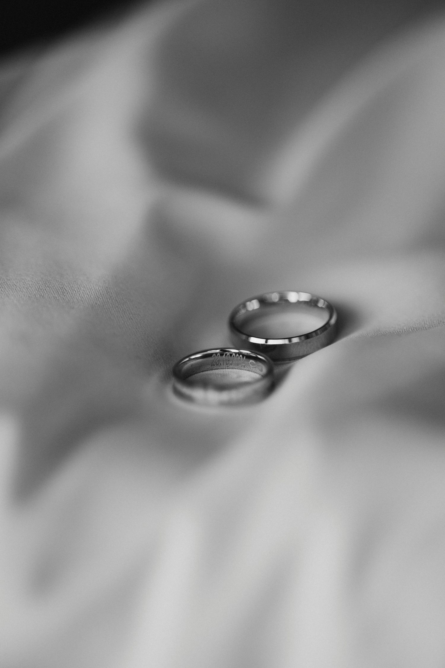 Two wedding rings placed on white silk fabric in black and white.