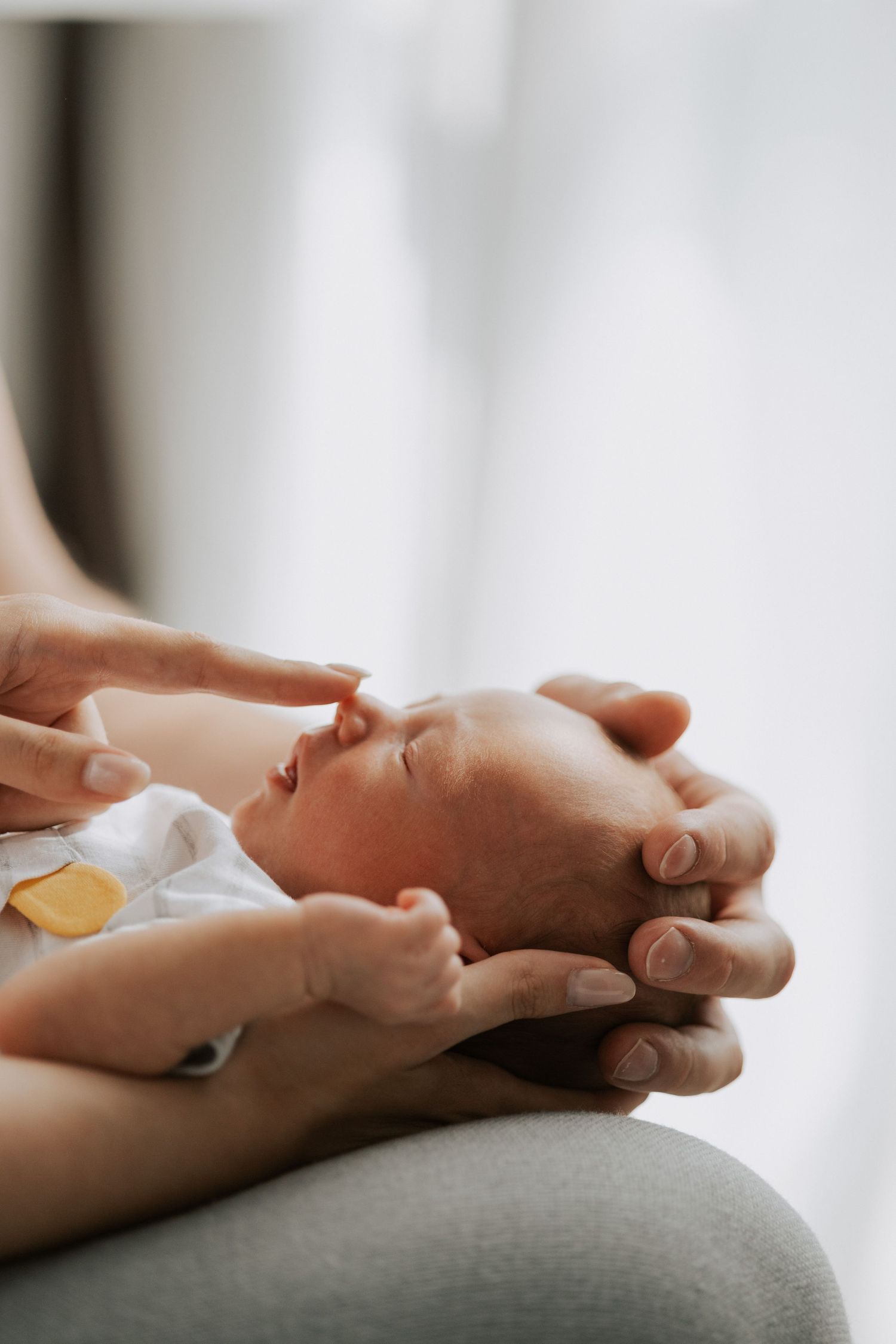 Gentle hands supporting a sleeping newborn baby's head against a light background.